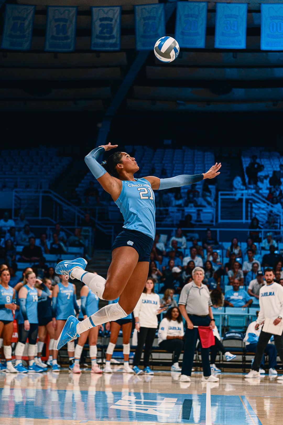 Volleyball player leaps to serve ball during competitive match at UNC.