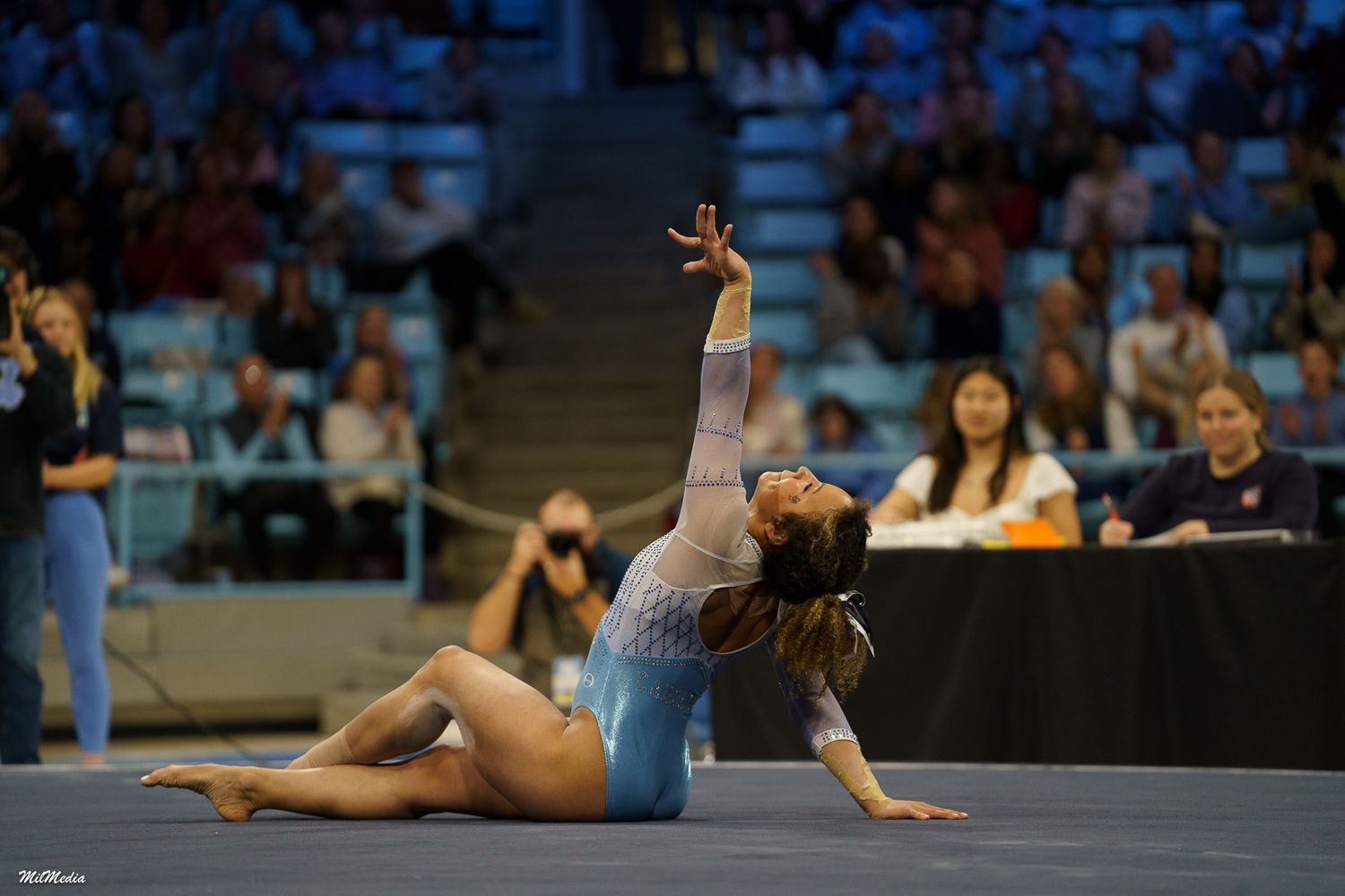 Gymnast performs an artistic floor routine in a light blue leotard at a competitive event.