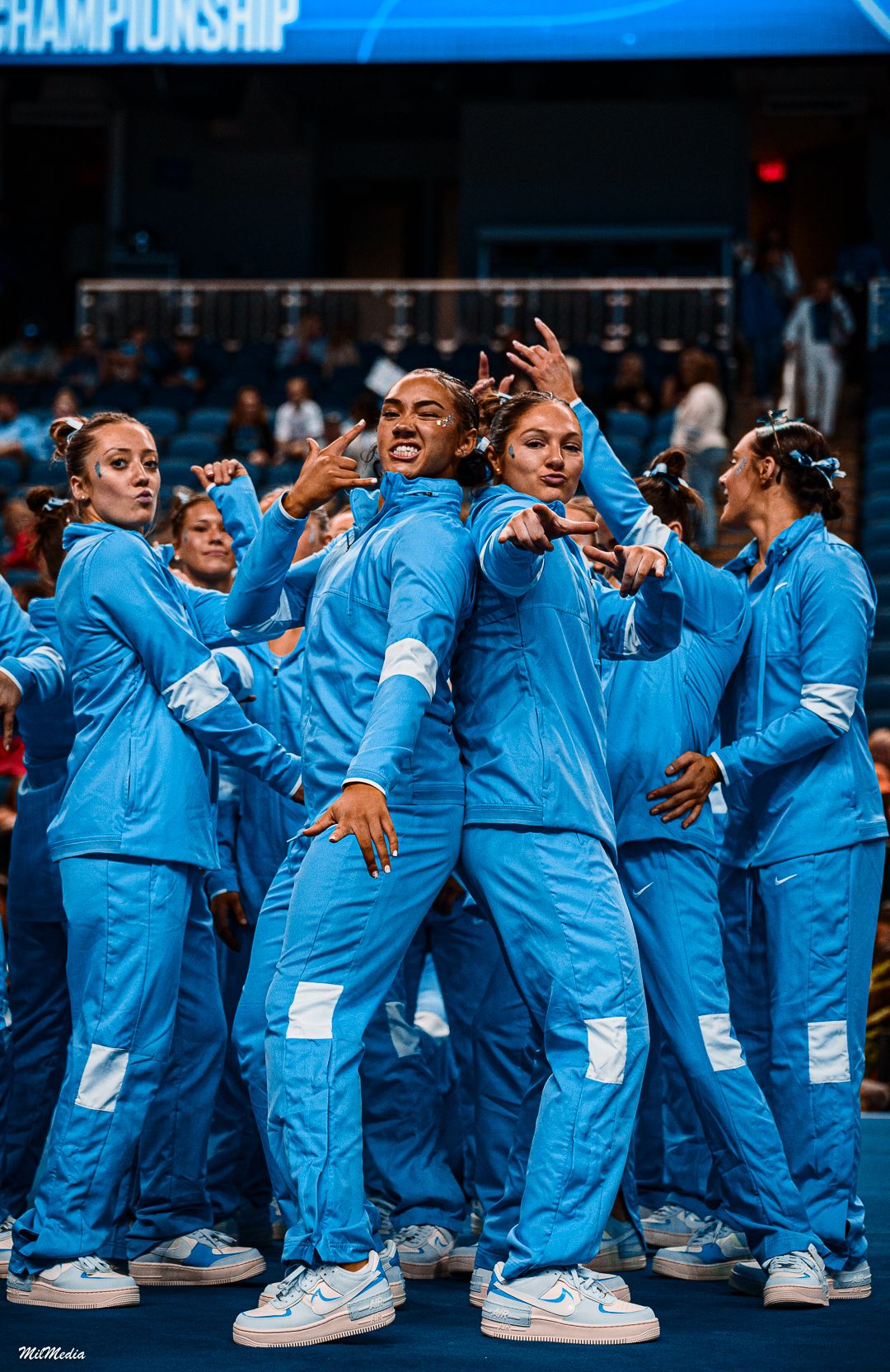 Team in matching blue tracksuits celebrates together at a gymnastics championship event.