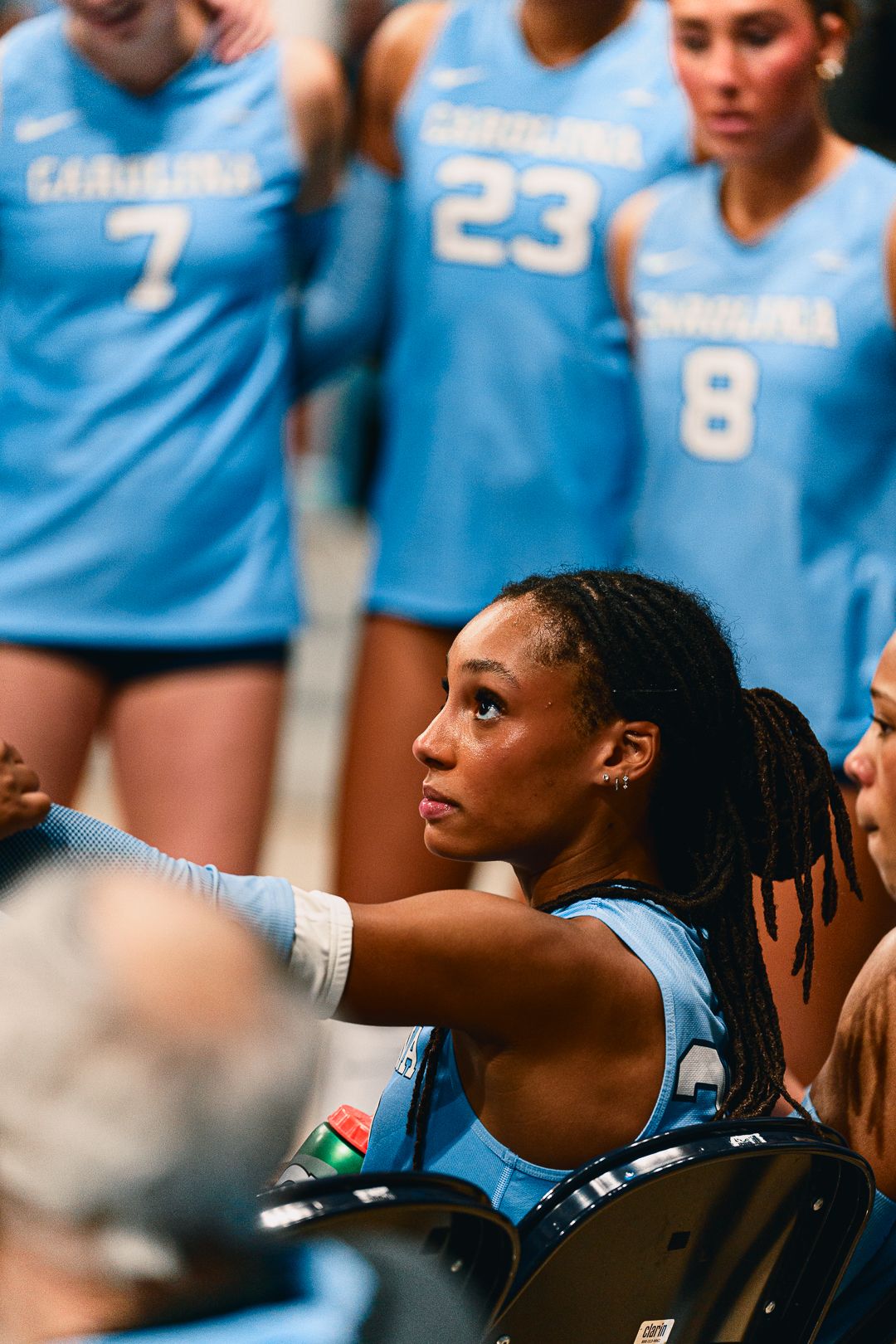 Players in light blue uniforms focus intently from the sidelines during a volleyball match.