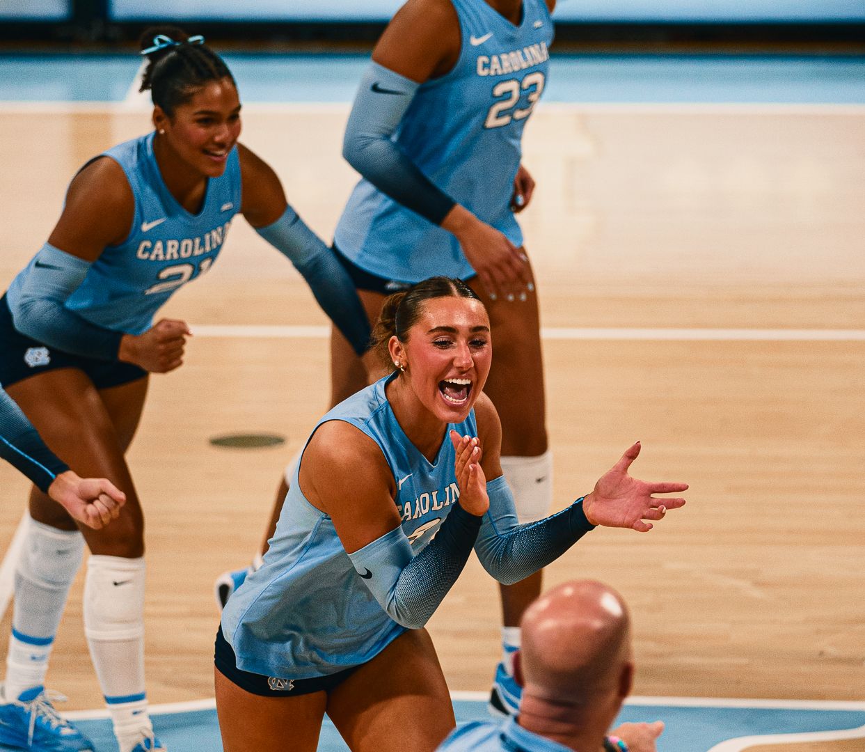 UNC Tar Heels women's volleyball player celebrates enthusiastically on court in light blue uniform during game.