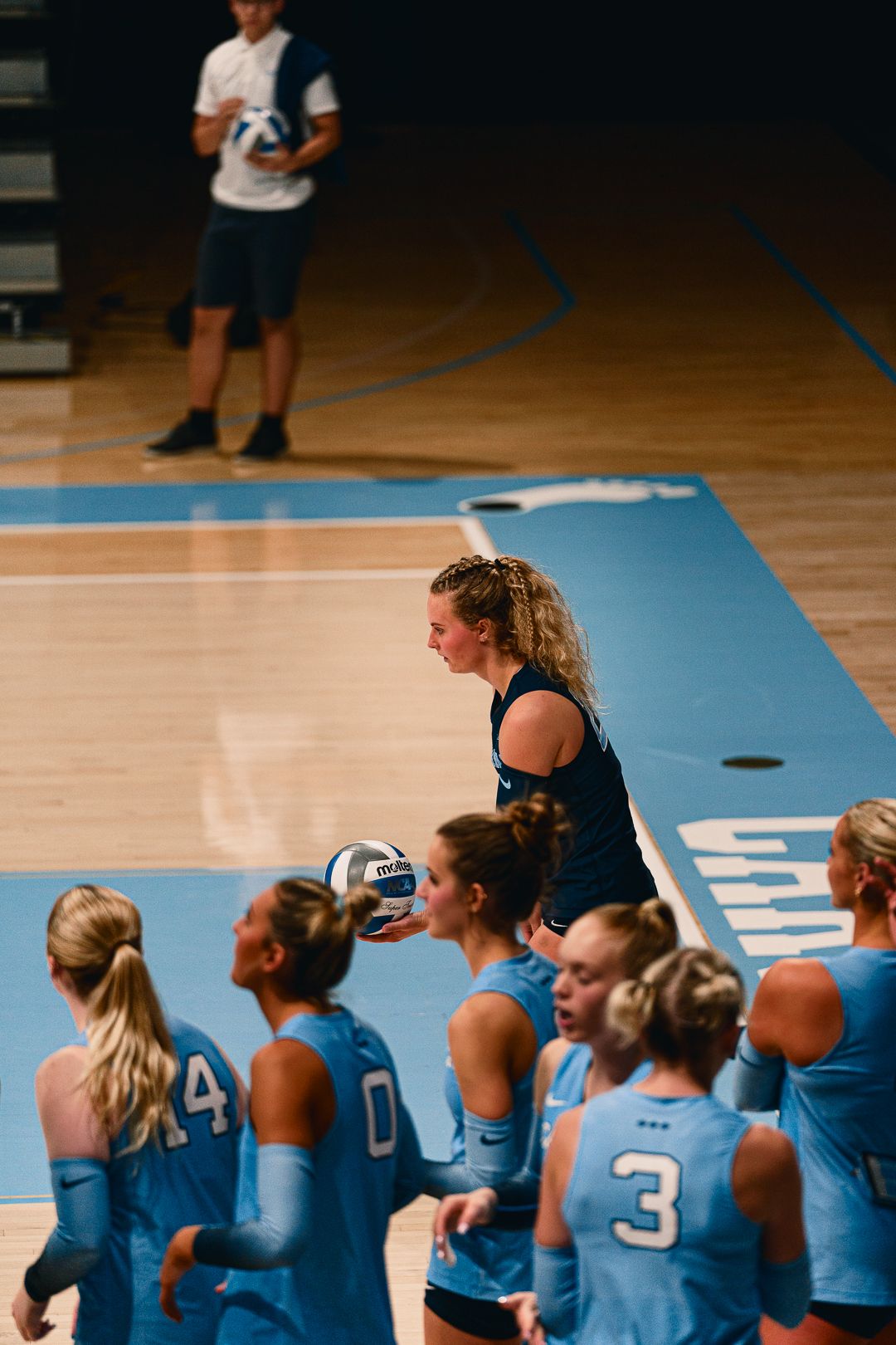 Volleyball team sits on bench during timeout while receiving coaching instructions.