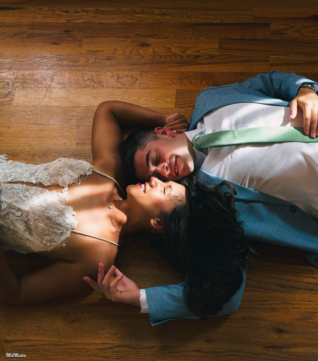 Couple in formal attire lying on hardwood floor in romantic pose.