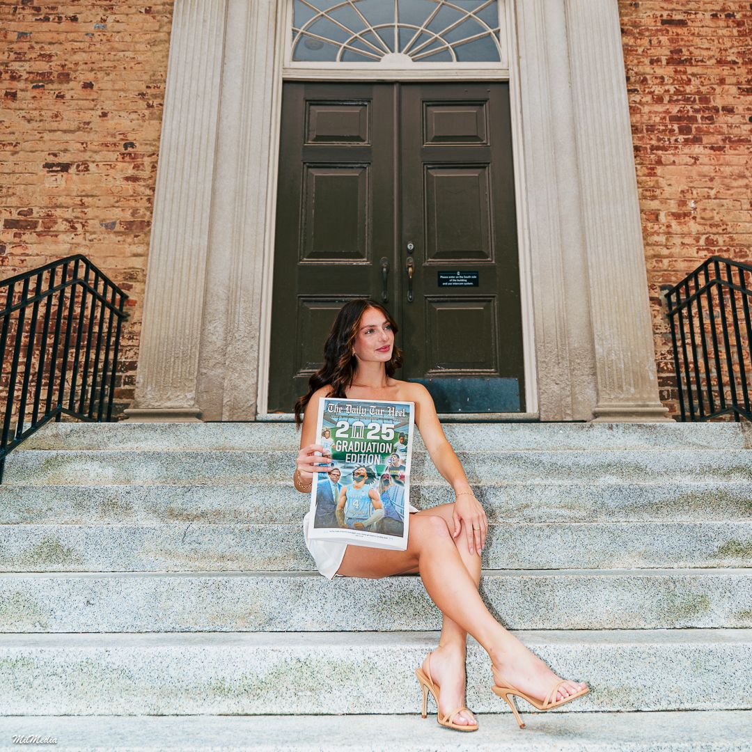 A person sits casually on stone steps in front of a historic brick building with multiple black doors.