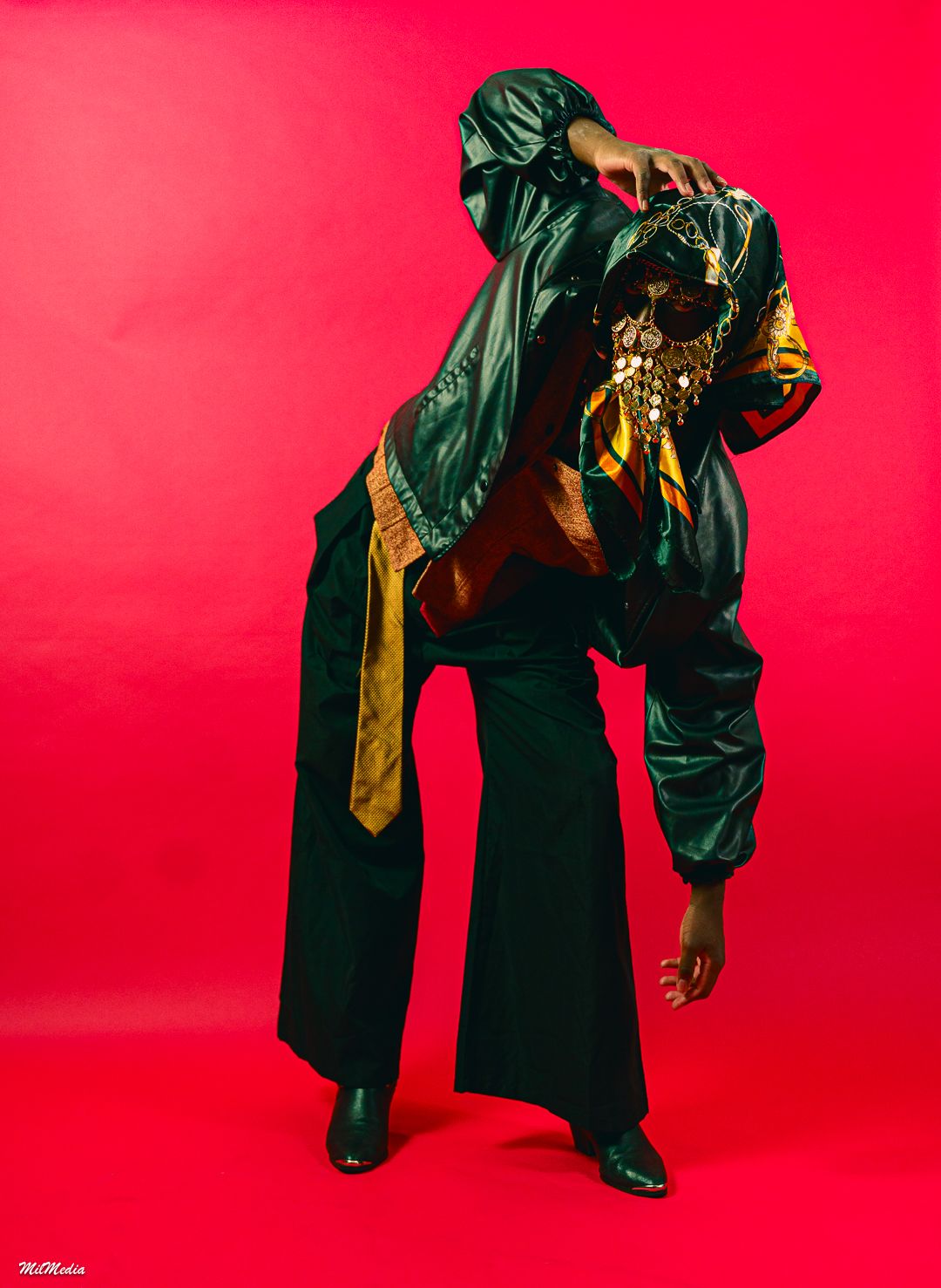Model in black and gold ensemble poses dramatically against vibrant red background.