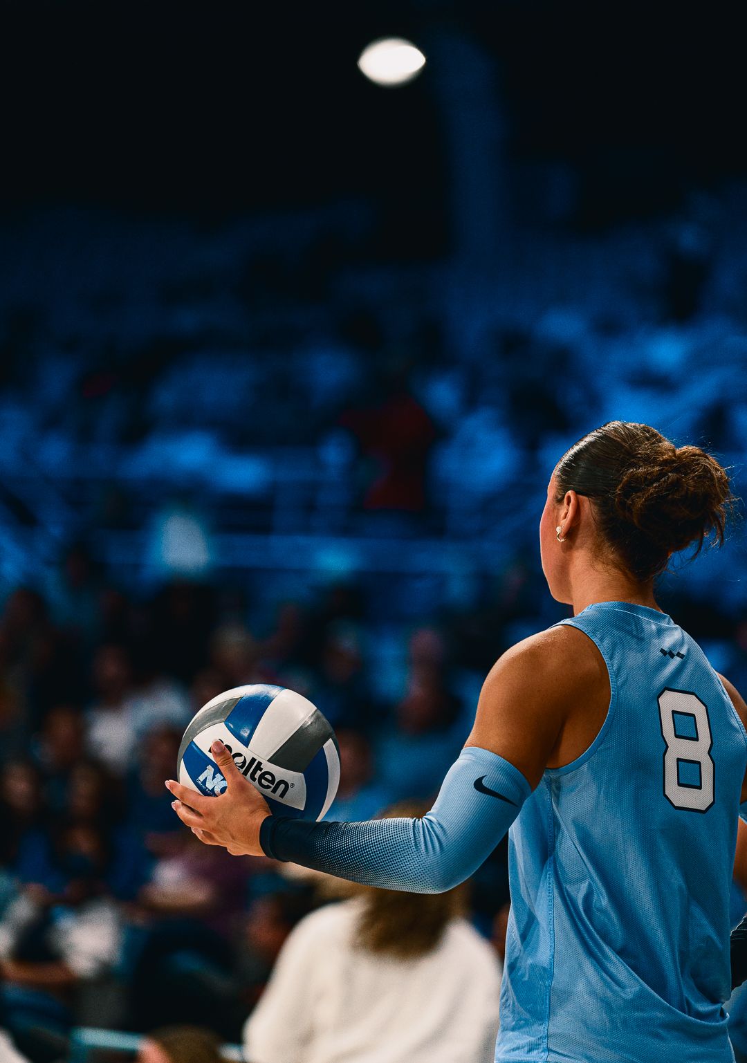 Volleyball players in light blue uniforms prepare to serve during a match.