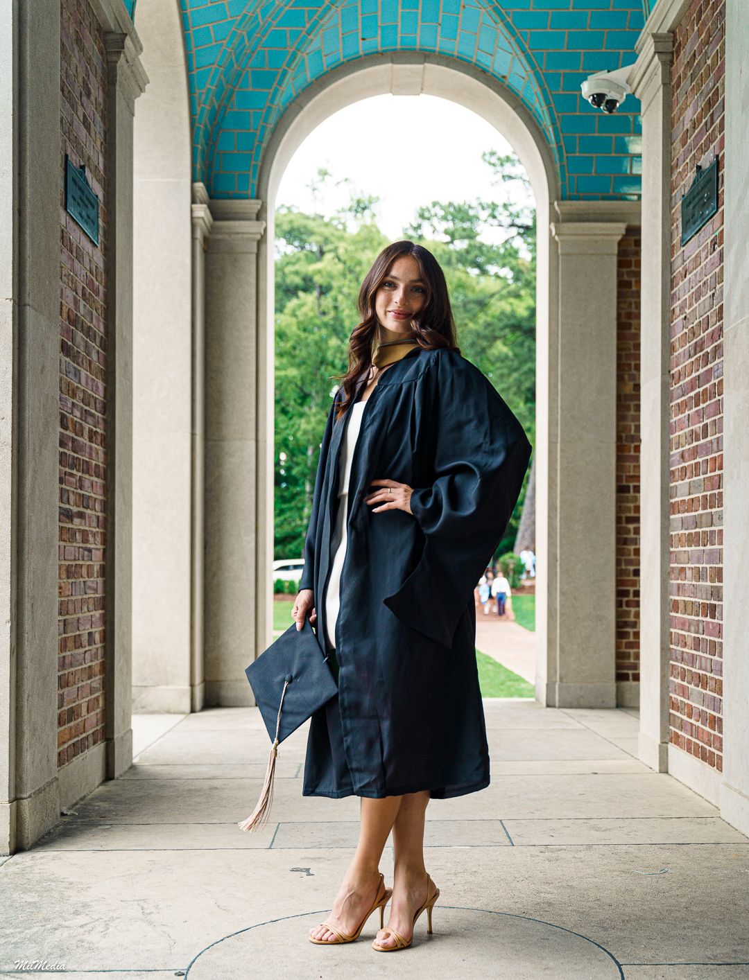 A person in graduation attire poses in the UNC Bell Tower.