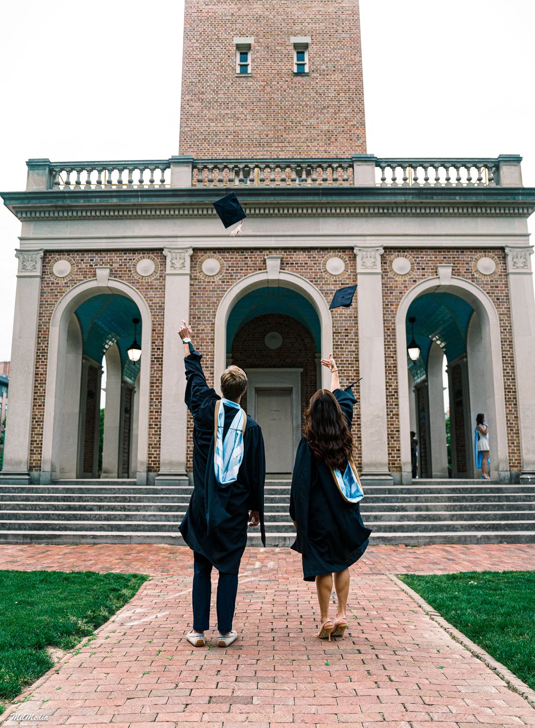 Two people in graduation attire pose in front of the UNC Bell Tower.