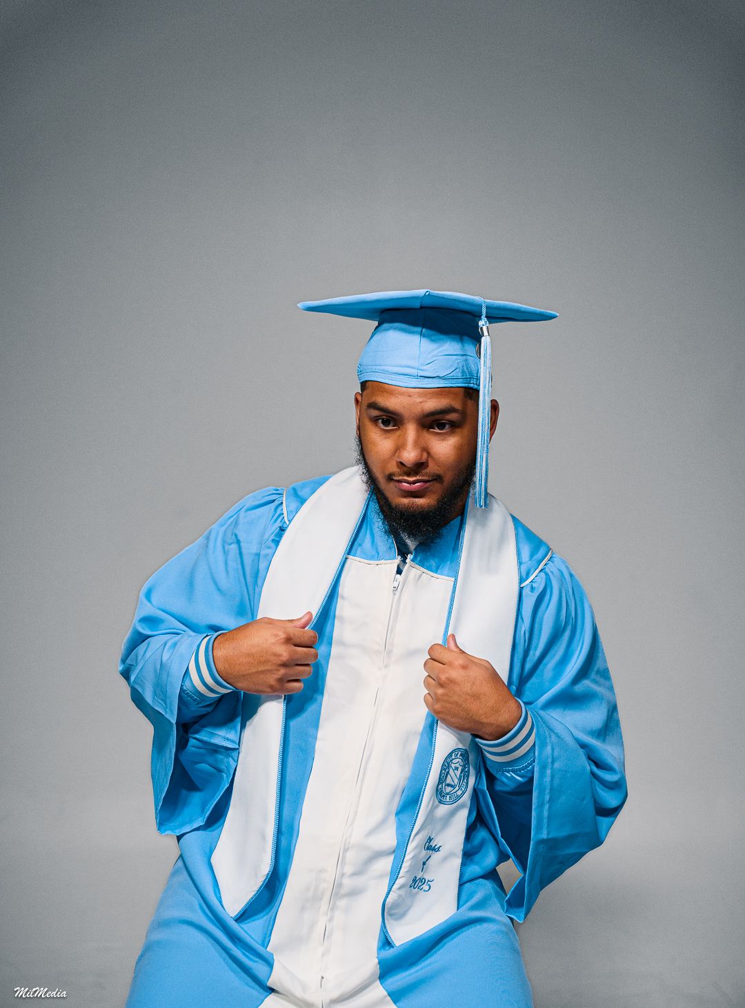 A graduate in UNC academic regalia poses expressively in a studio setting.