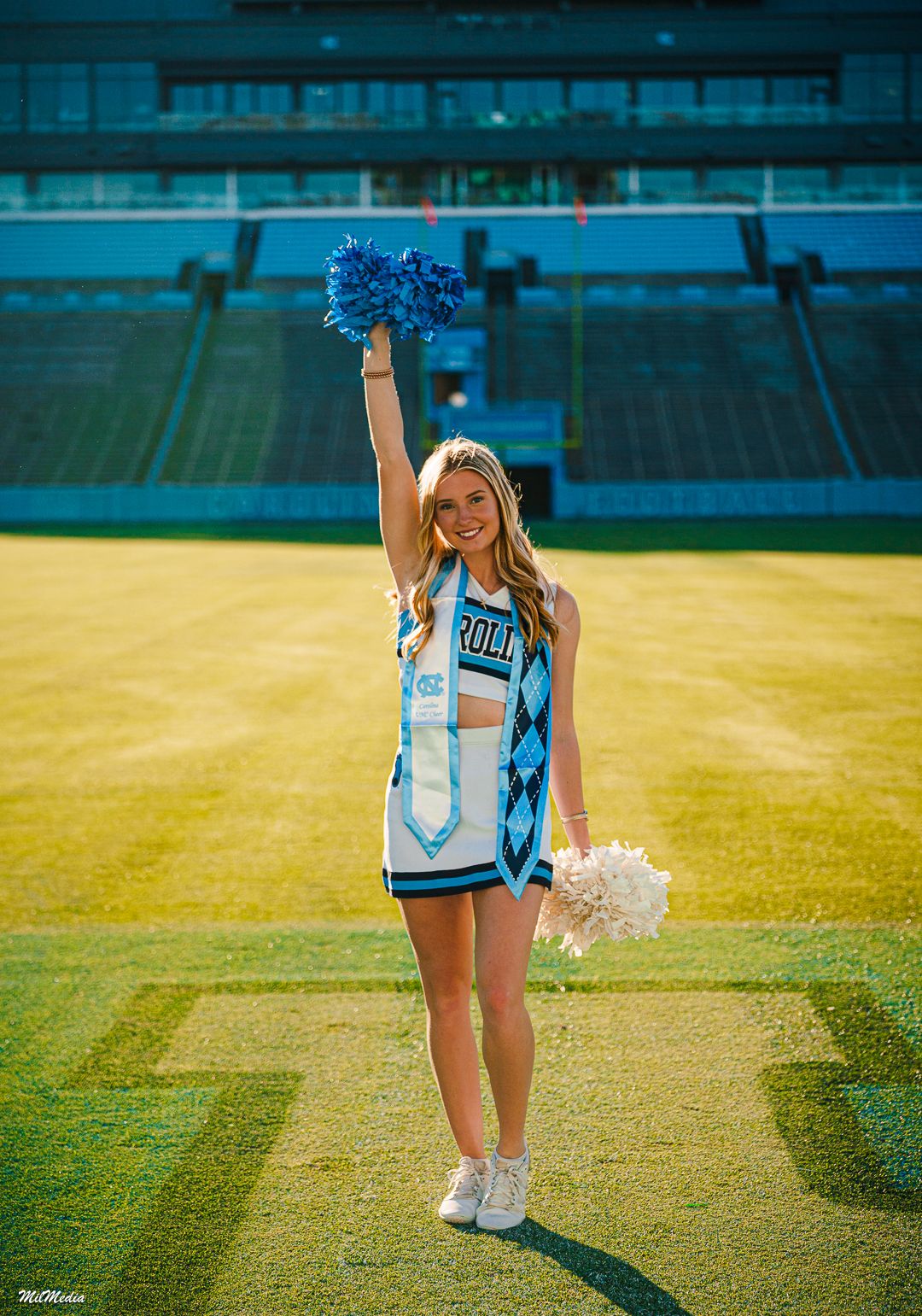 Cheerleader poses at Kenan Stadium with blue stadium seats in background.