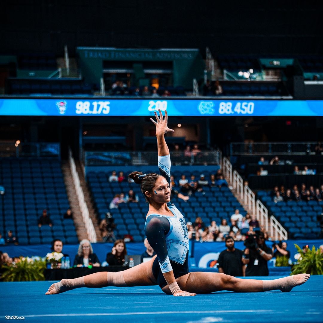 Gymnast executes split pose during floor routine at collegiate competition.