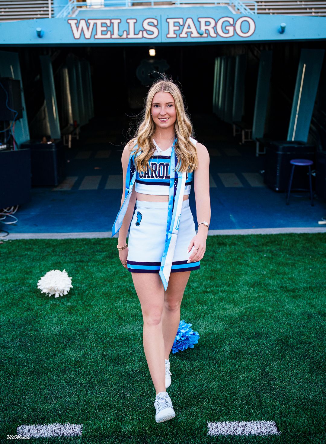 UNC Cheerleader poses with pom poms at Kenan Stadium near Wells Fargo signage.