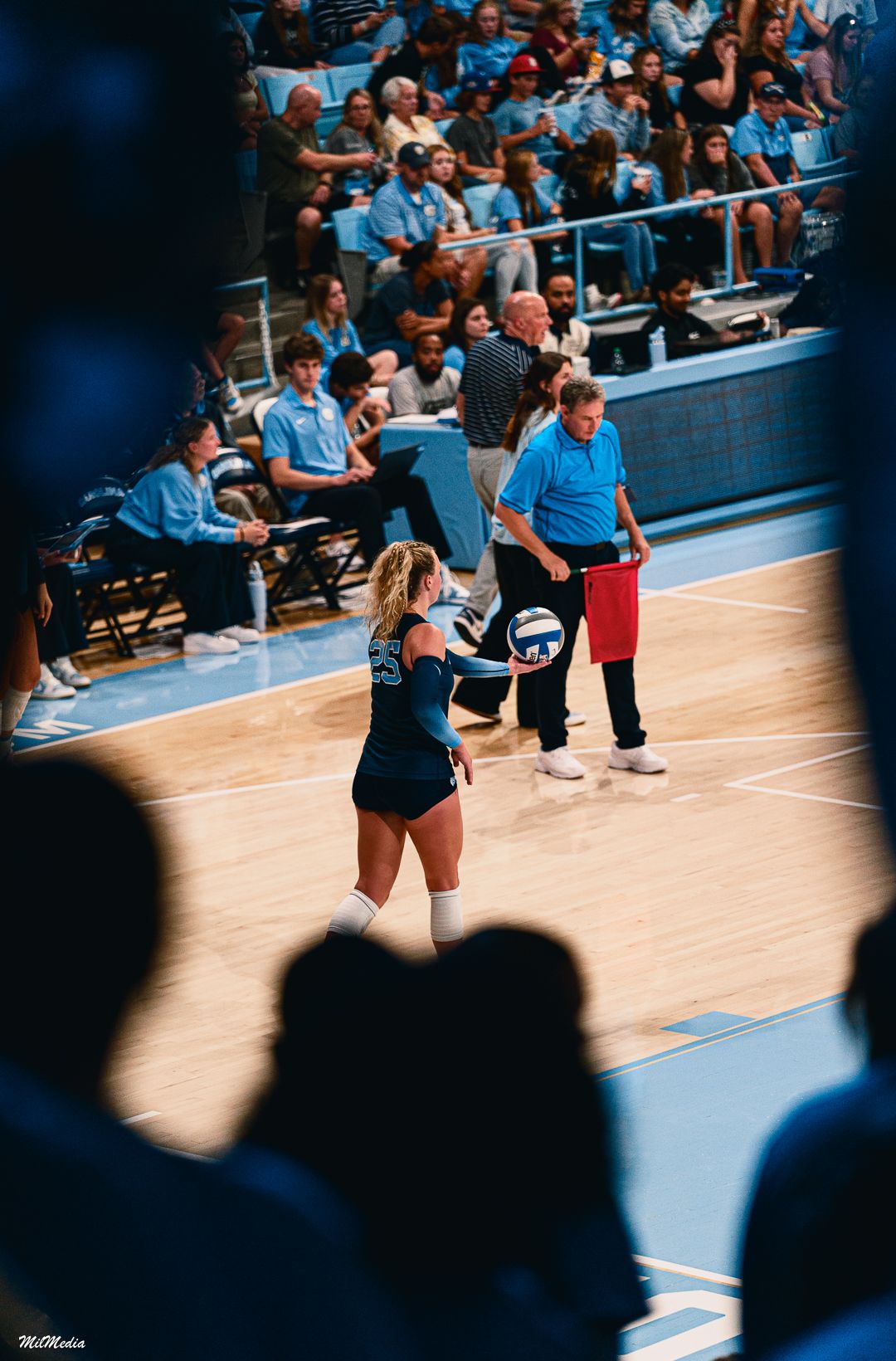 Volleyball match in progress at UNC arena with crowd silhouettes visible.