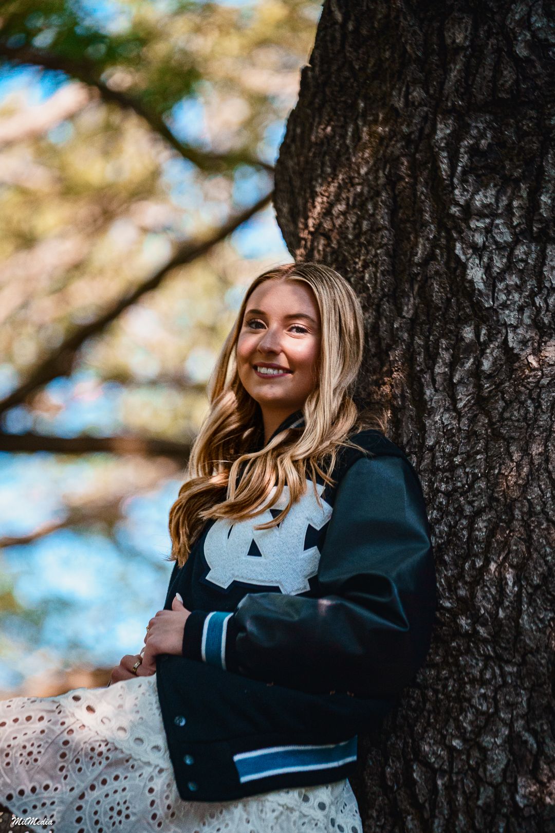 Outdoor portrait session against tree trunk with natural sunlight filtering through leaves.