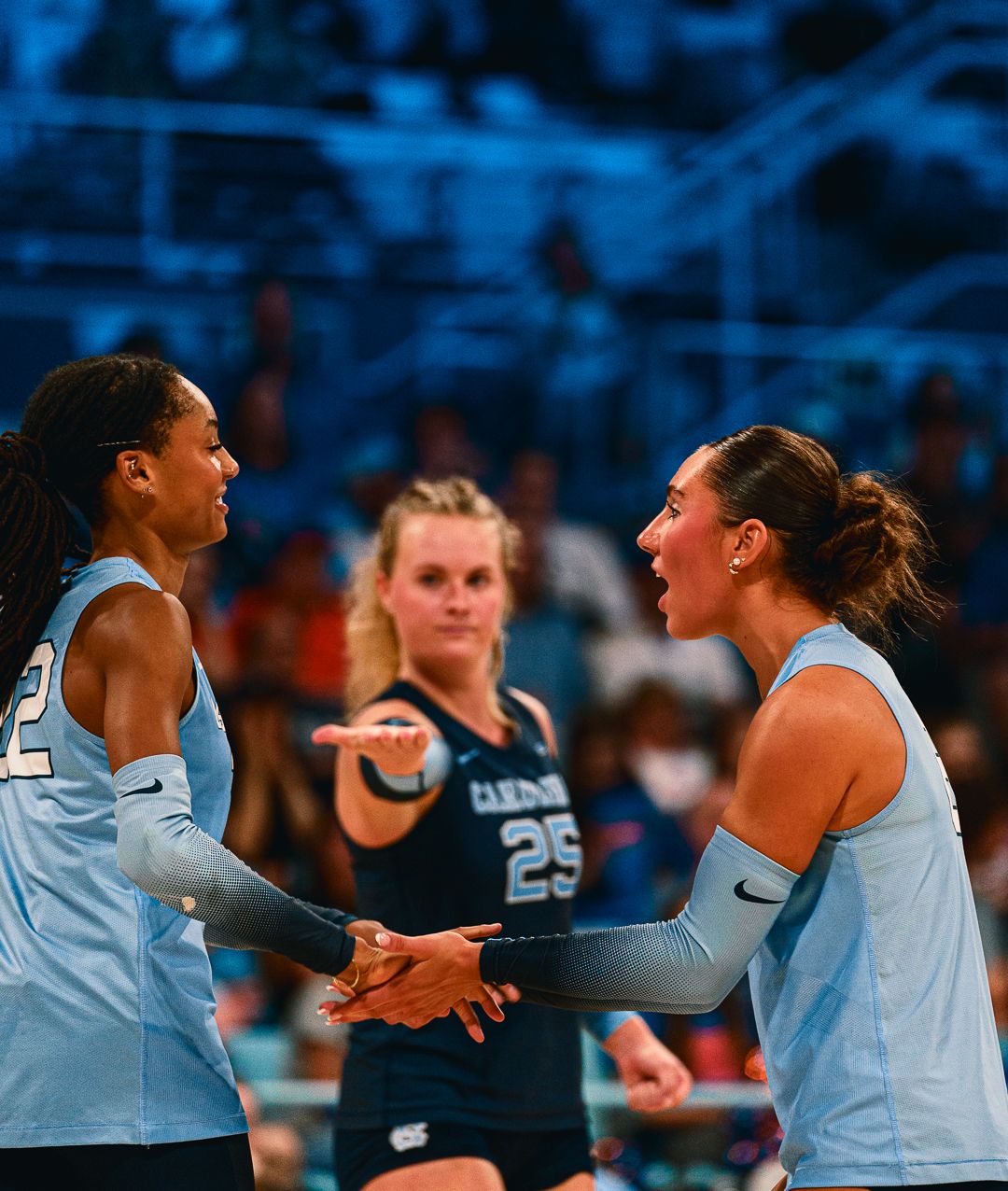 Teammates in Carolina blue jerseys celebrate together during an intense volleyball match.