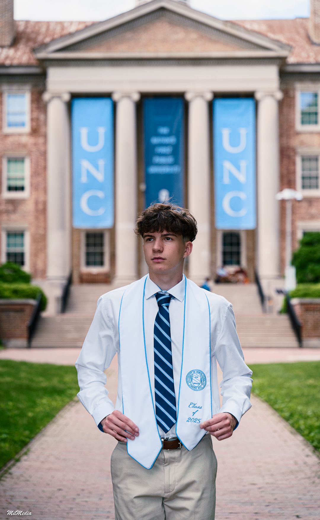 A graduation photo in front of UNC campus building with blue banners and classical columns.