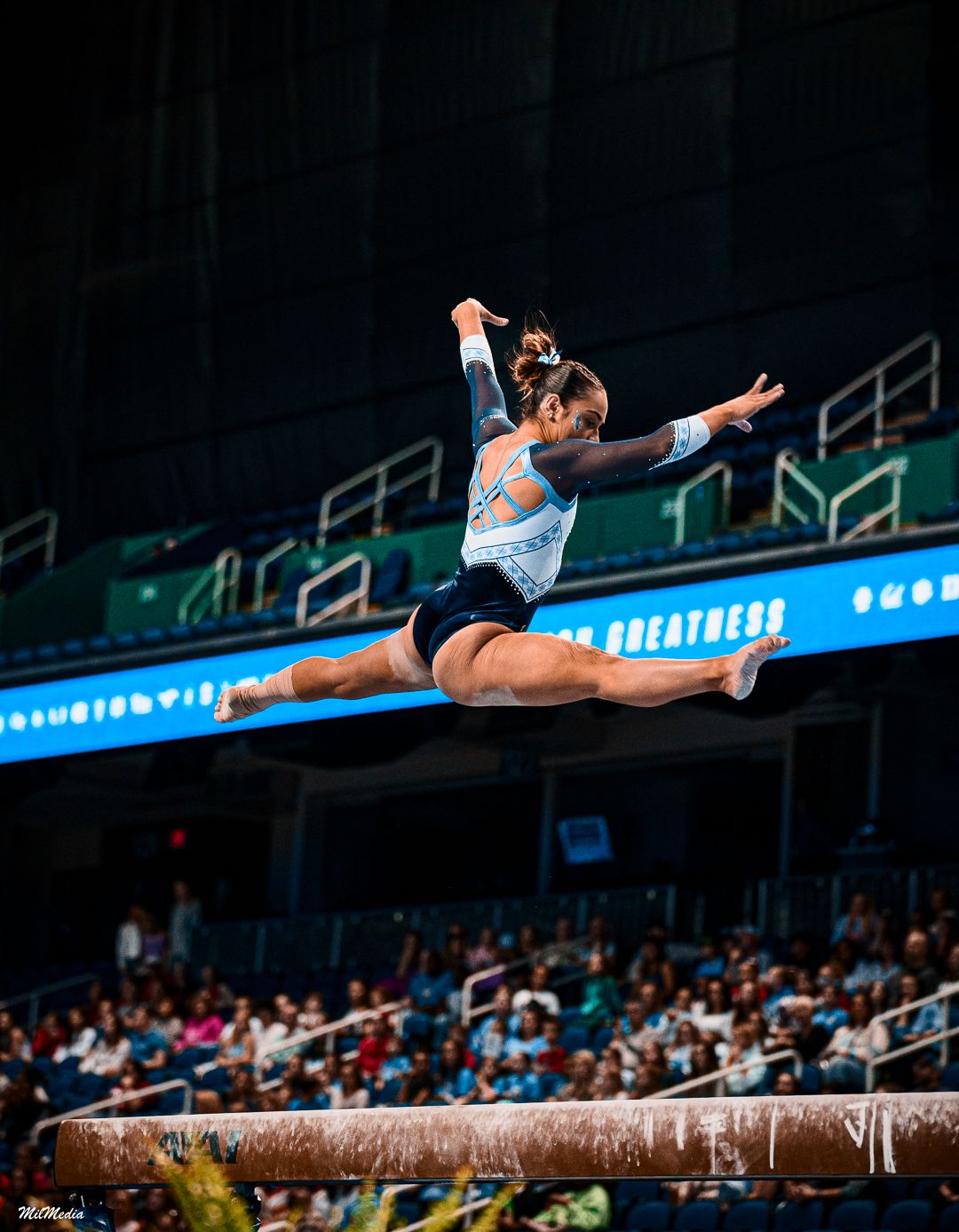 Gymnast performs split leap on balance beam during competition.