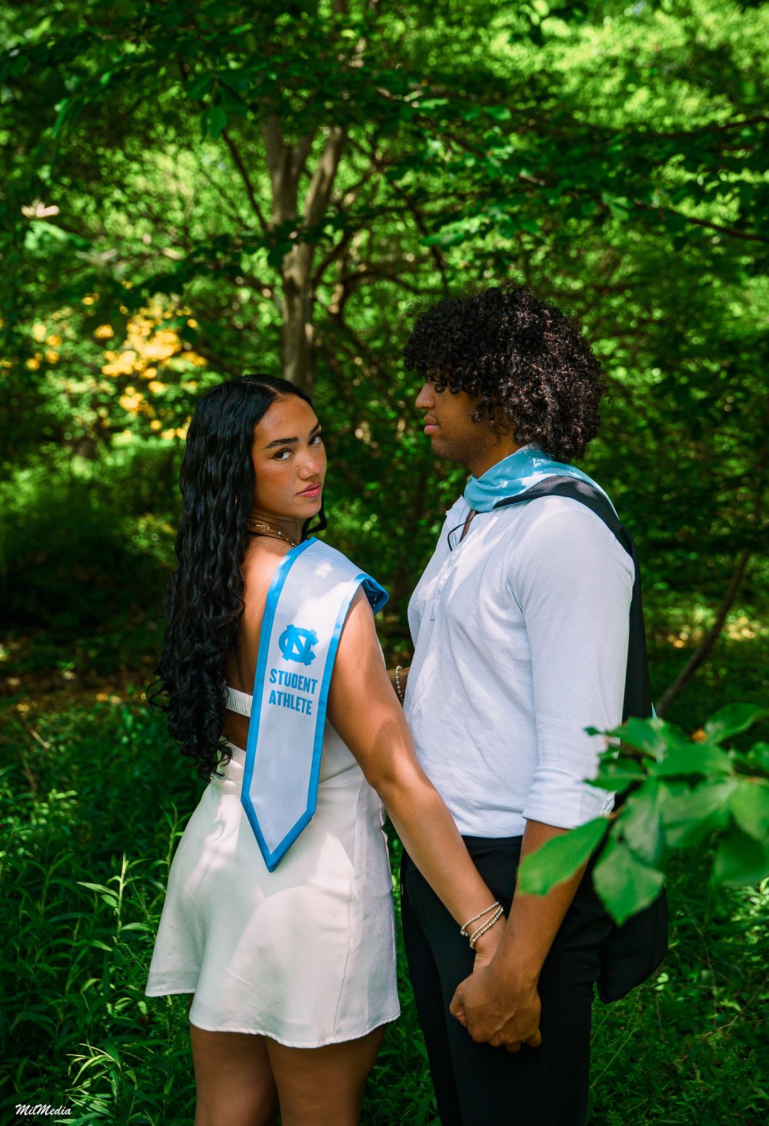 Graduation photoshoot in a lush green garden setting with light blue graduation sashes.