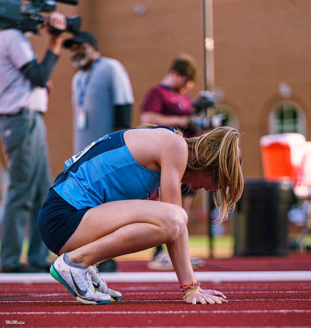 Runner dives dramatically towards finish line on red track during competitive race during the ACC Track and Field Championships.
