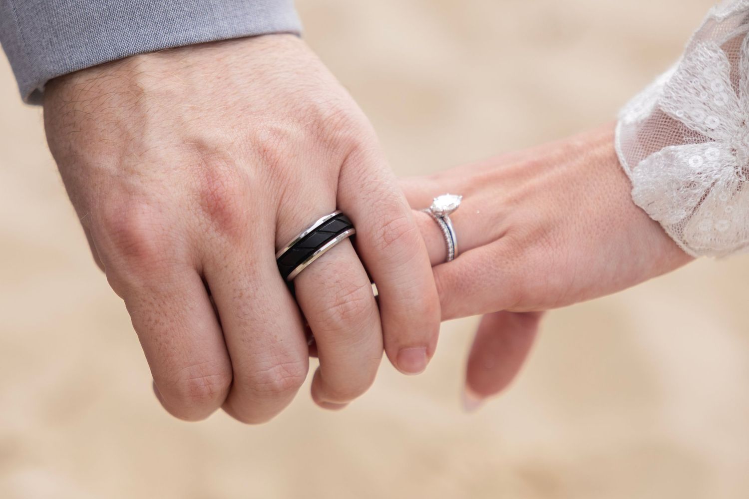 Close-up of couple holding hands on beach, wearing matching wedding bands, symbolizing love and commitment.