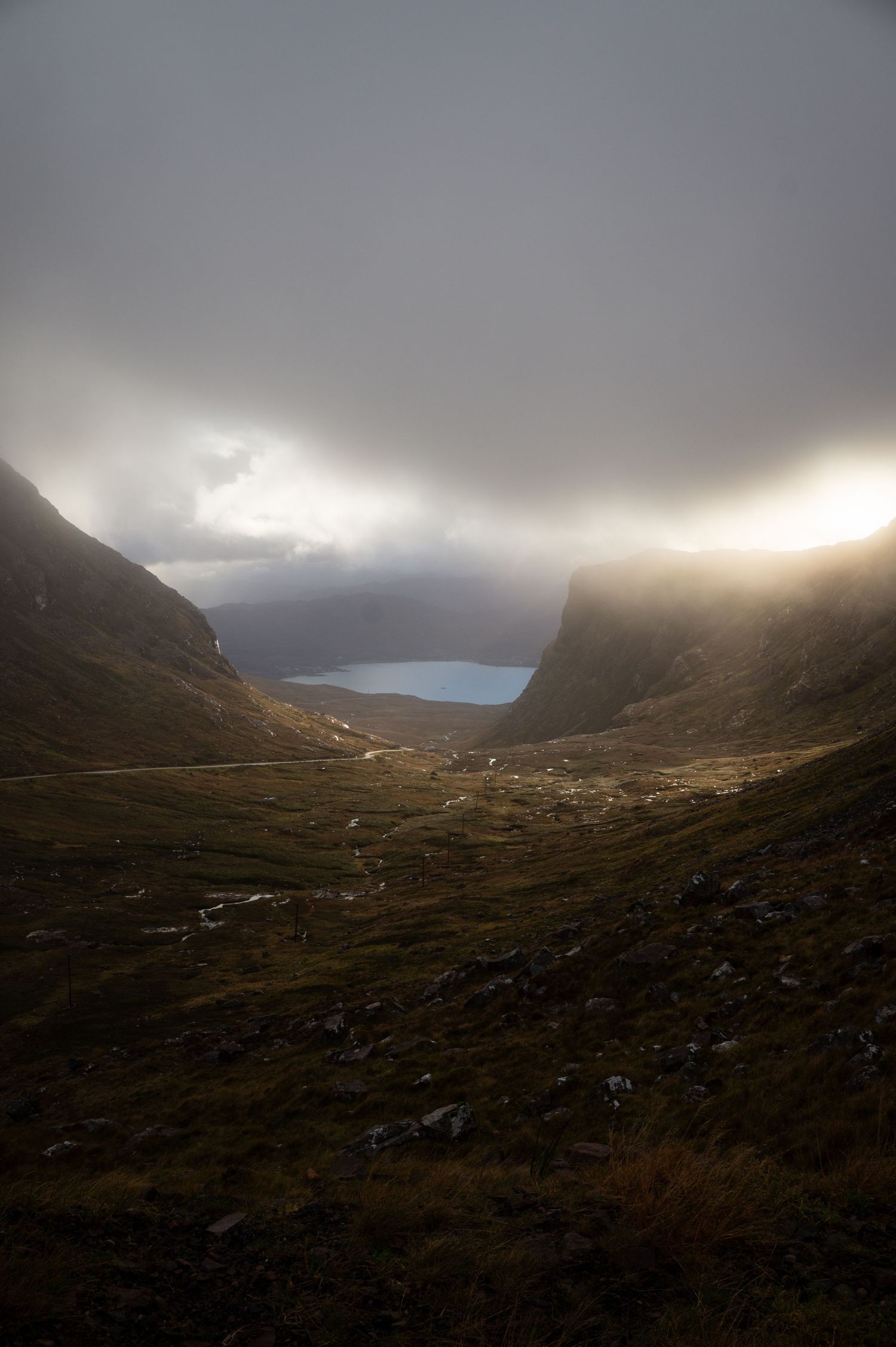 Vue sur la vallée et la route menant au Bealach na Bà en Ecosse avec les rayons du soleil qui percent un nuage.