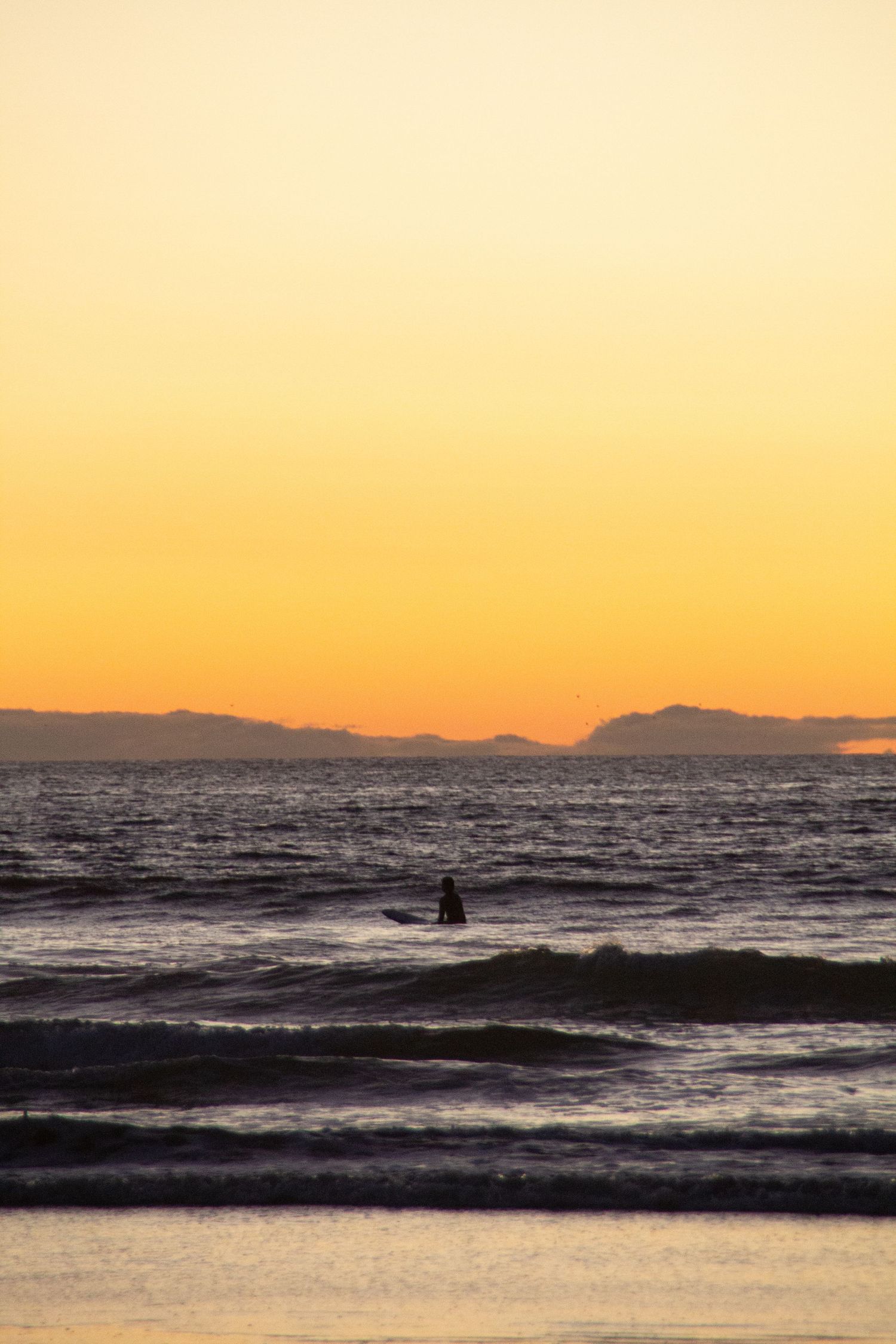 Surfeur assis sur sa planche dans l’eau sous un coucher de soleil orange.