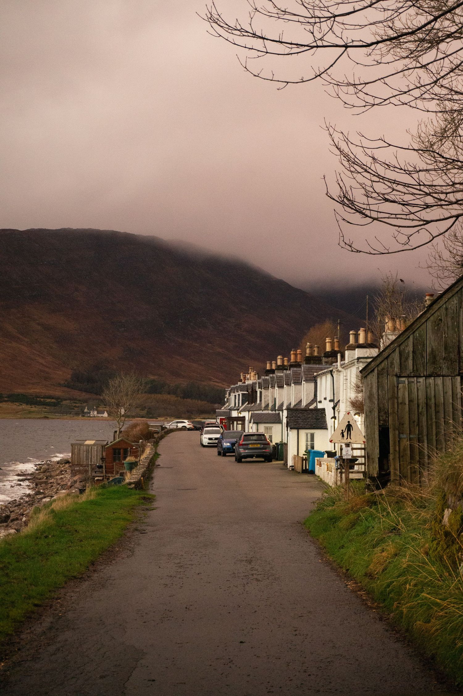 Route traversant le village d’Applecross en Ecosse avec la mer à gauche, les maisons de pêcheurs à droite et la montagne en arrière plan.