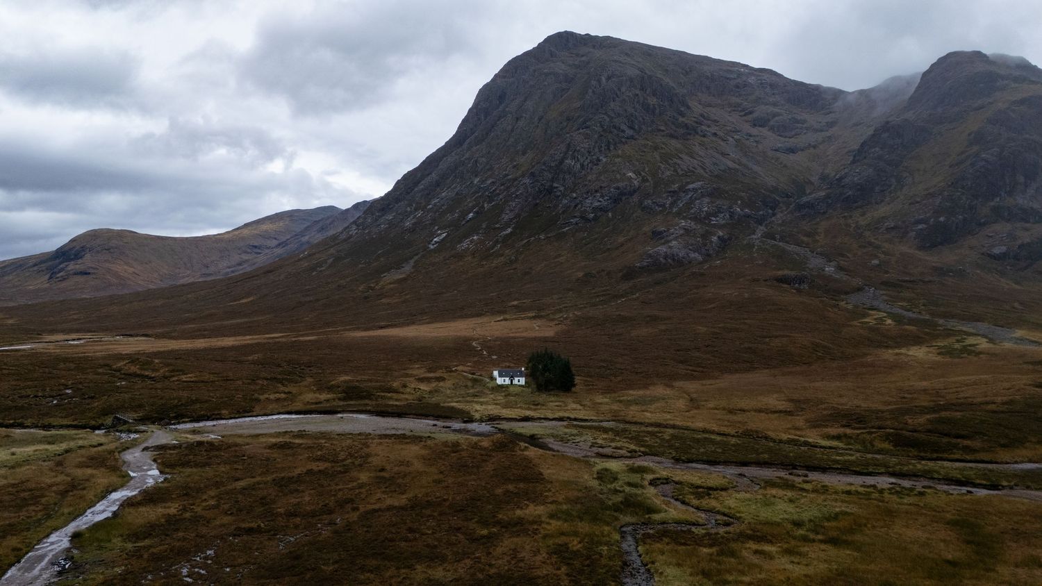 Vue aérienne de la maison blanche emblématique de Glencoe avec des montagnes en arrière plan.
