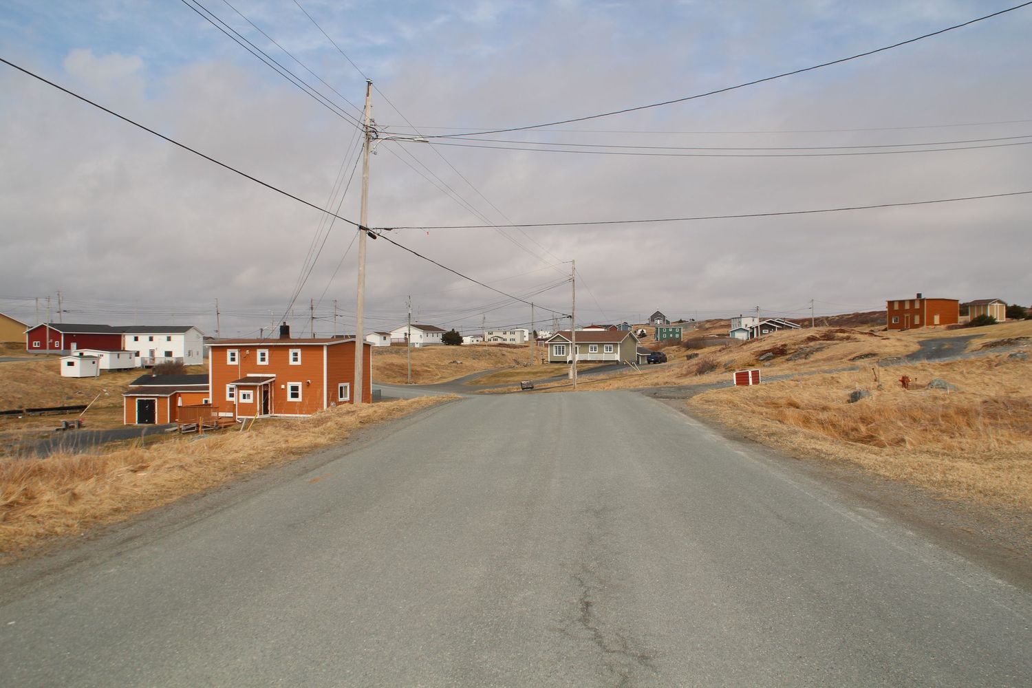 Route qui traverse un village de Terre Neuve et ses maisons colorées bordées de pelouse sèche
