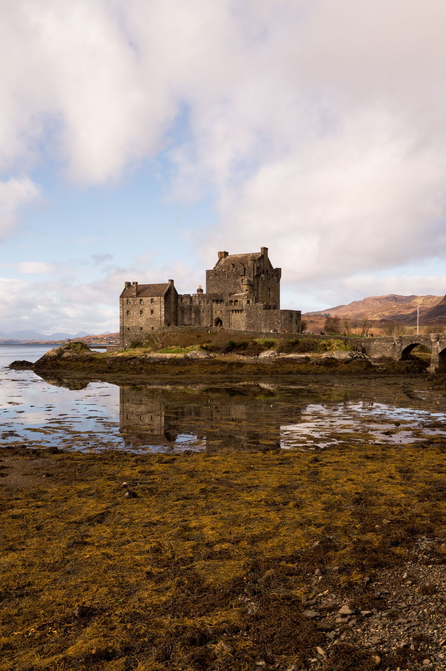 Chateau Eilean Donan entouré d’une mer partiellement basse révélant herbes et roches.