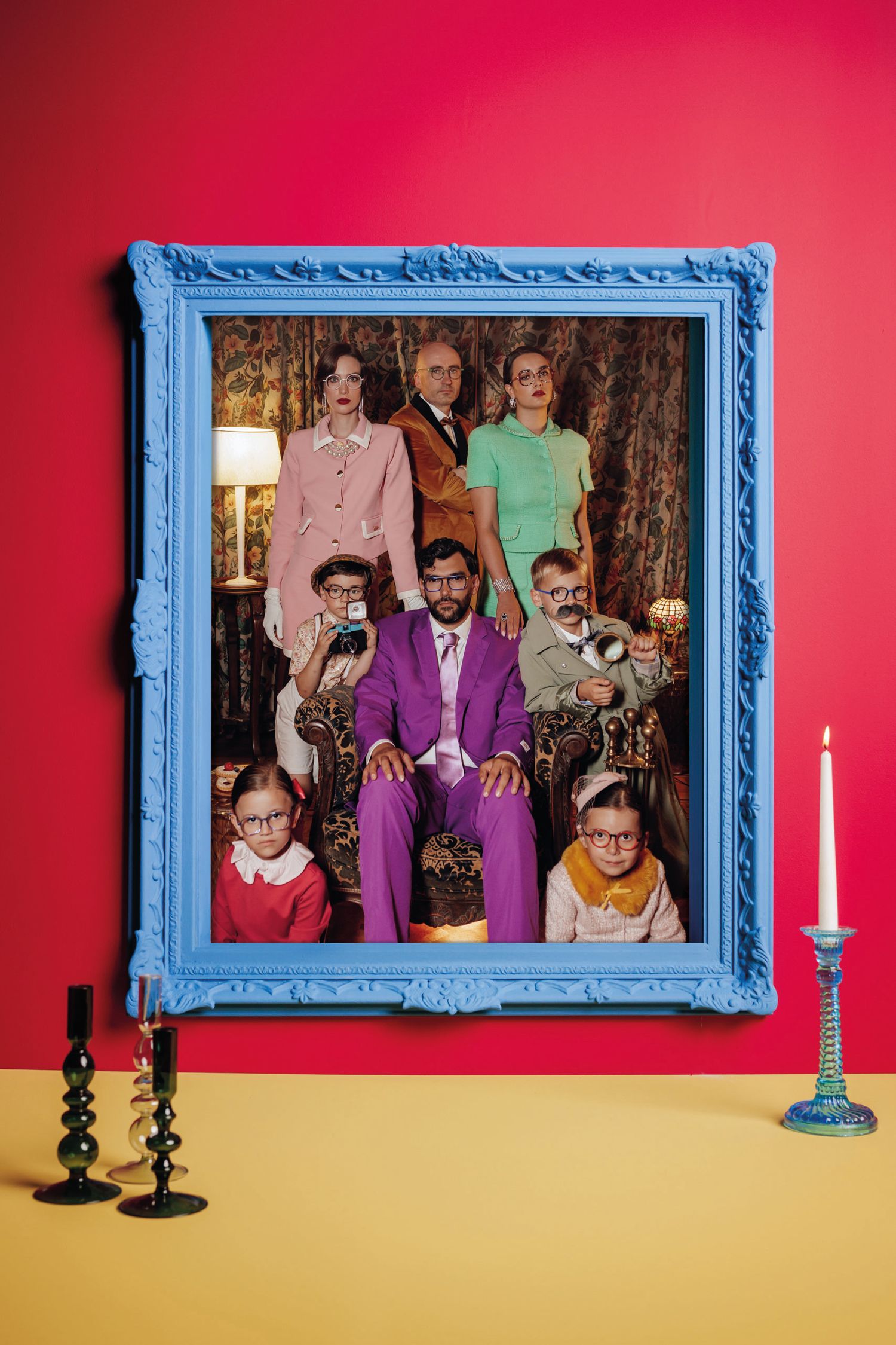 Portrait d’une famille habillée à la mode des années folles, dans un cadre bleu sur un mur rouge