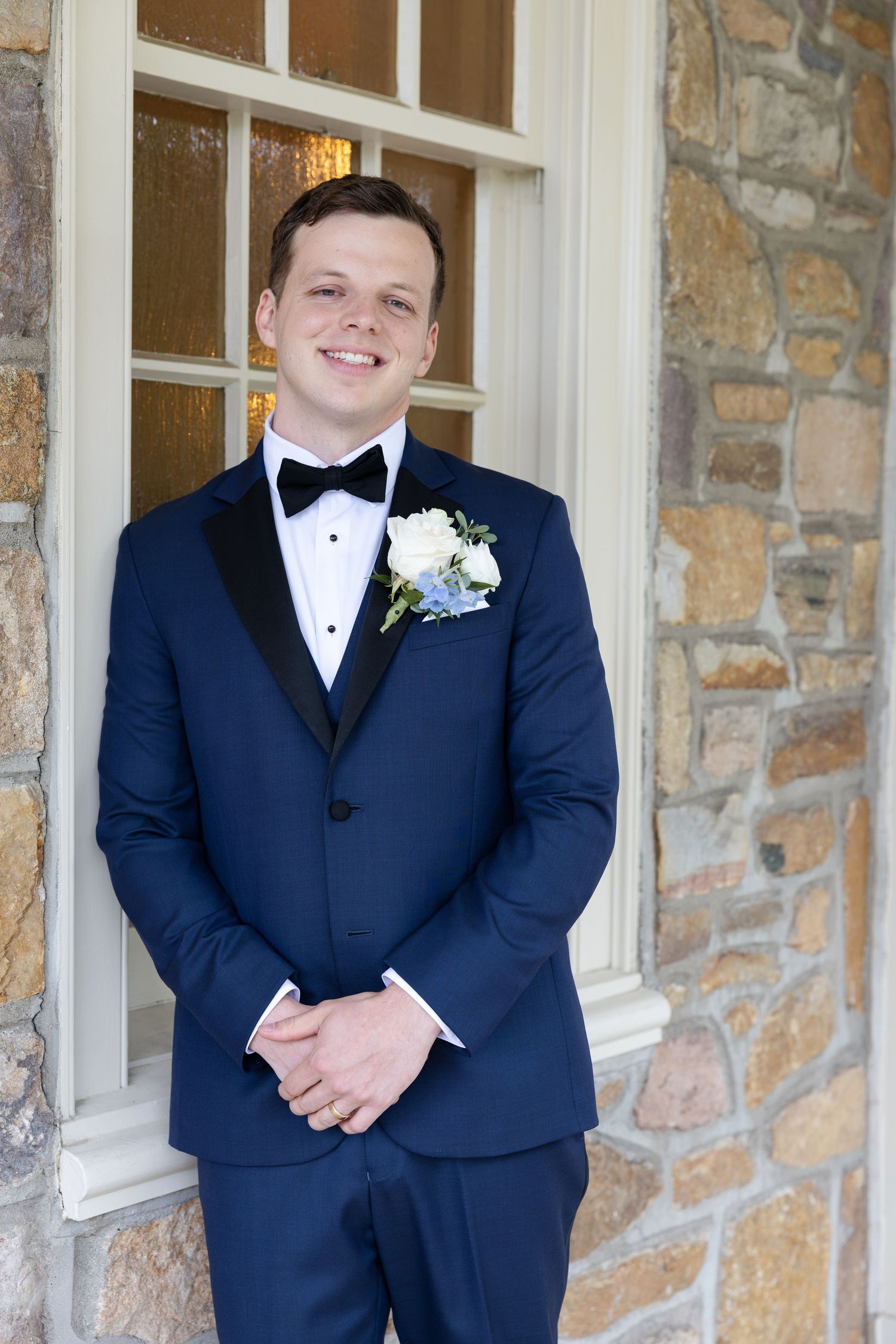Groom portrait in navy tuxedo against stone building exterior.