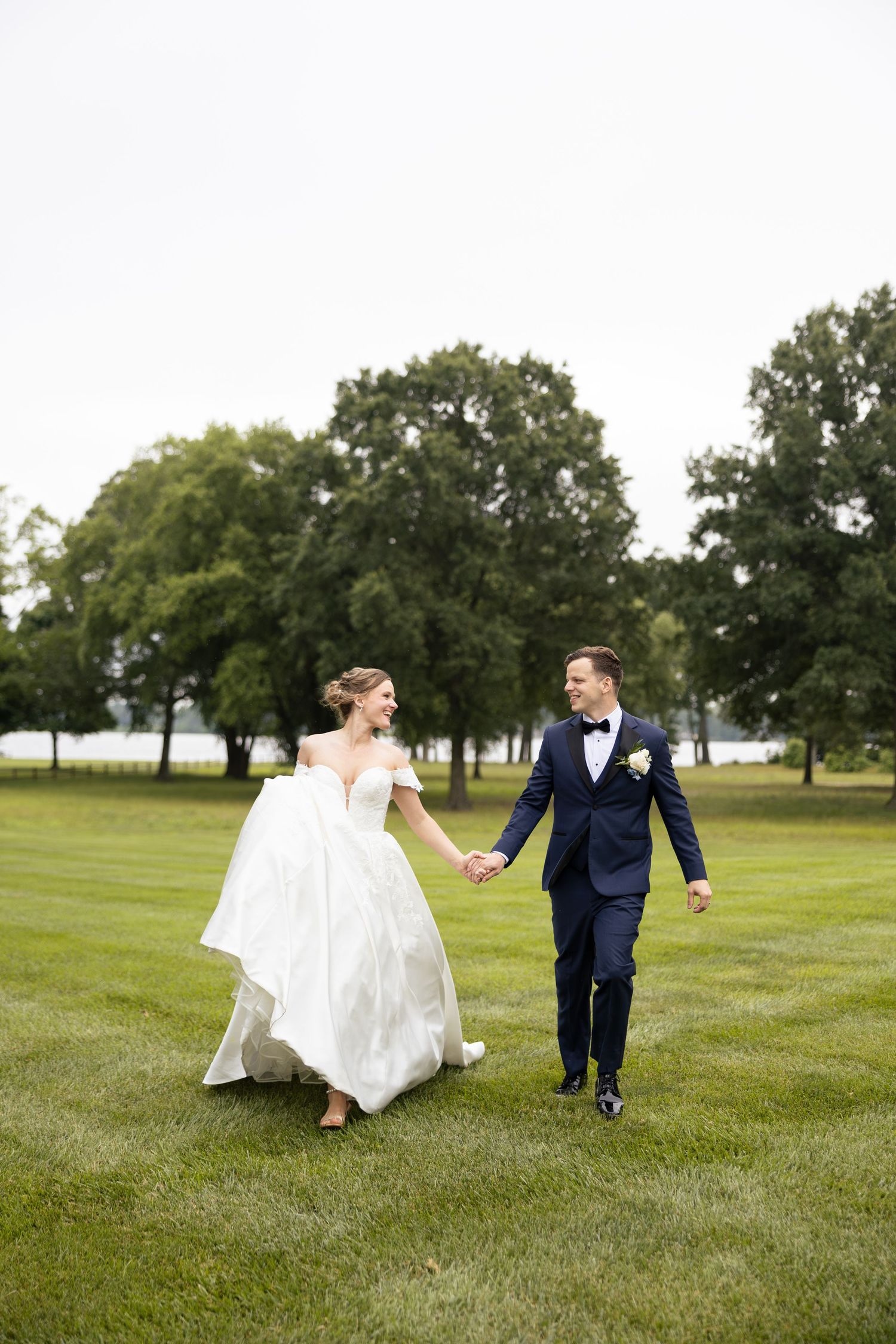 Couple running and playing together on grassy field in wedding attire.