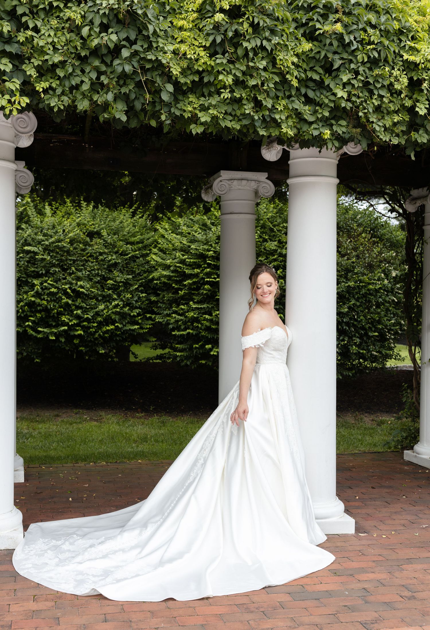 Bride in flowing white gown poses under classical white columned portico.
