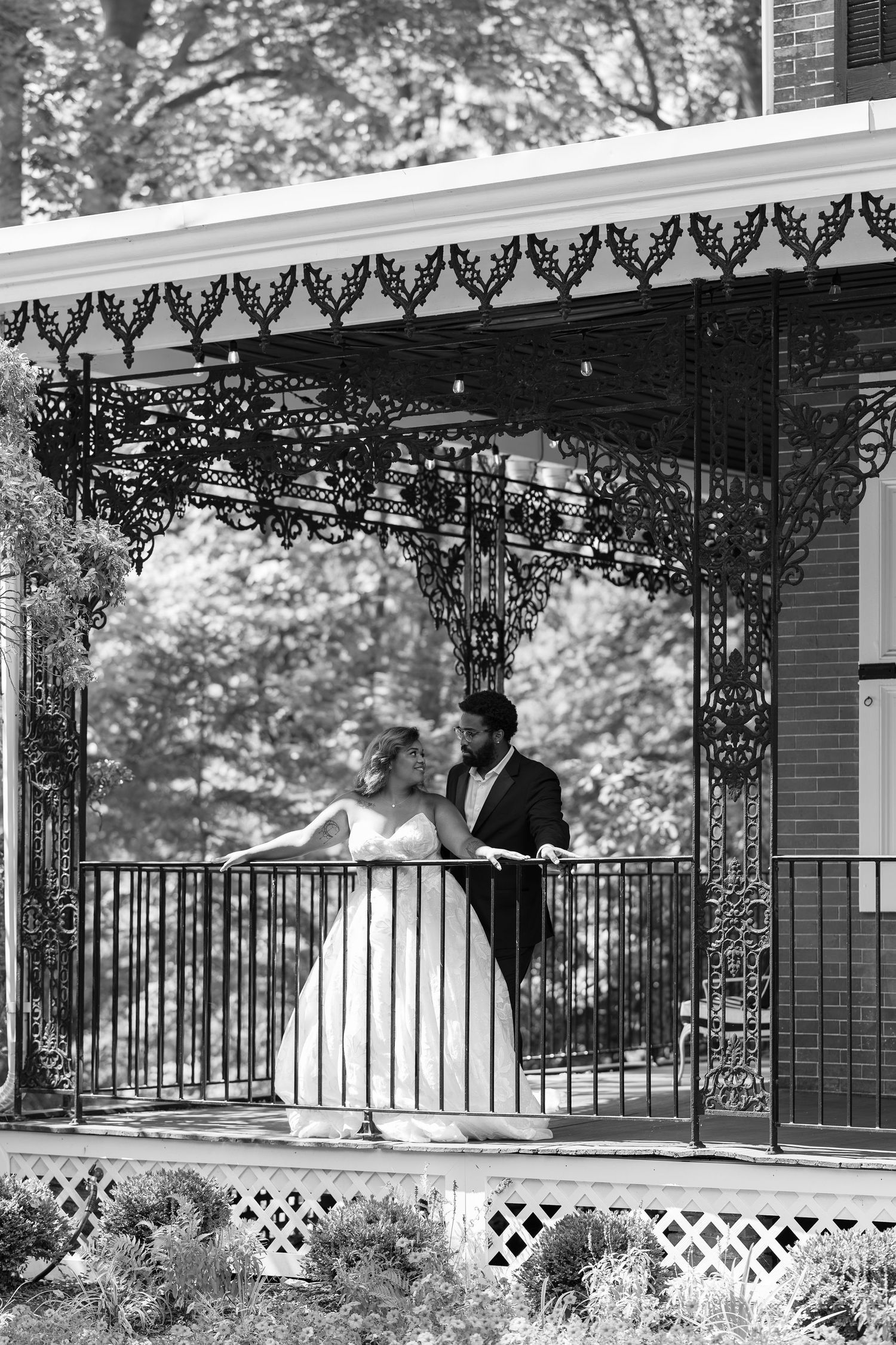 Wedding couple stands under ornate Victorian gazebo in black and white photograph.