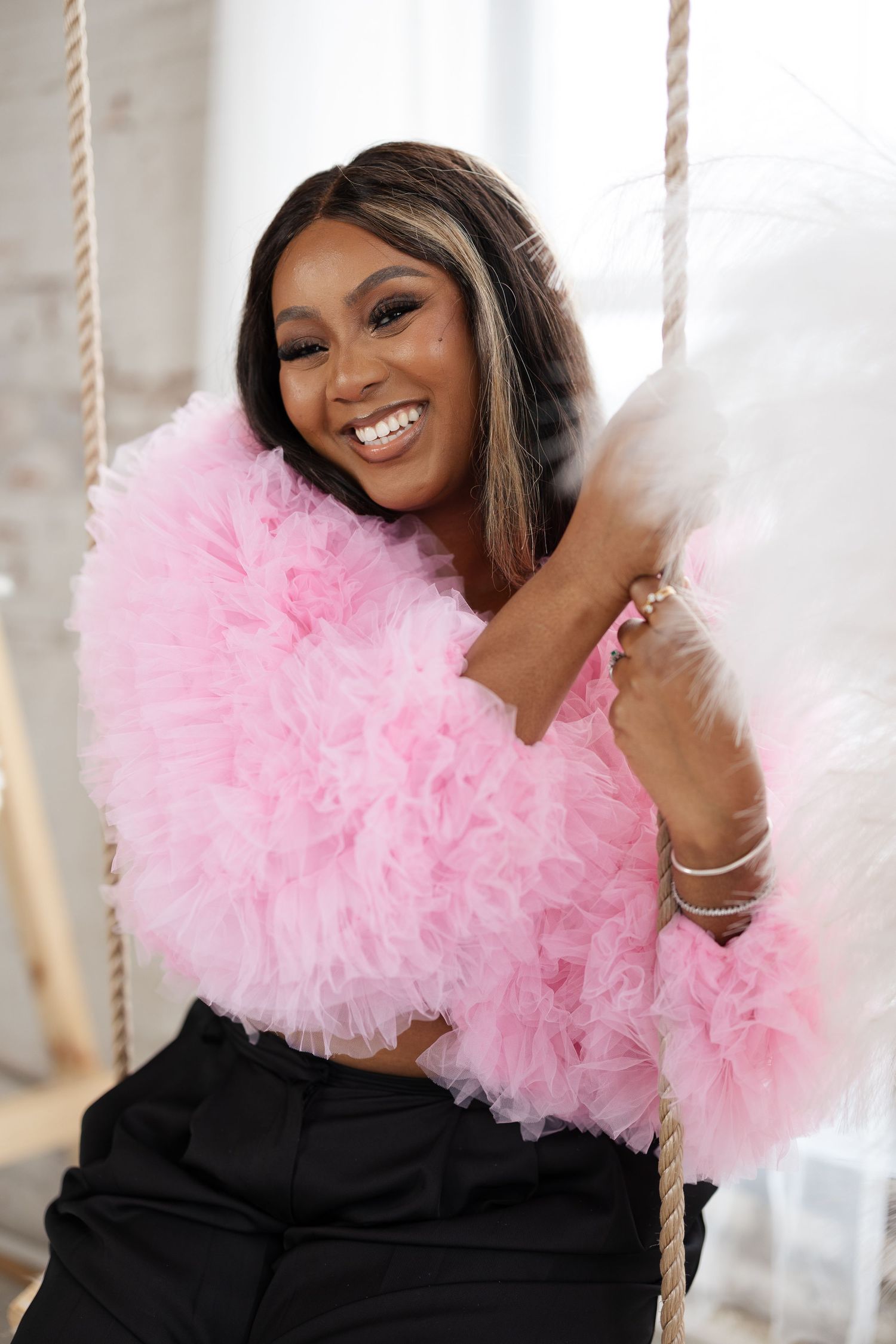 Joyful portrait featuring pink tulle jacket and elegant black pants on decorative swing.