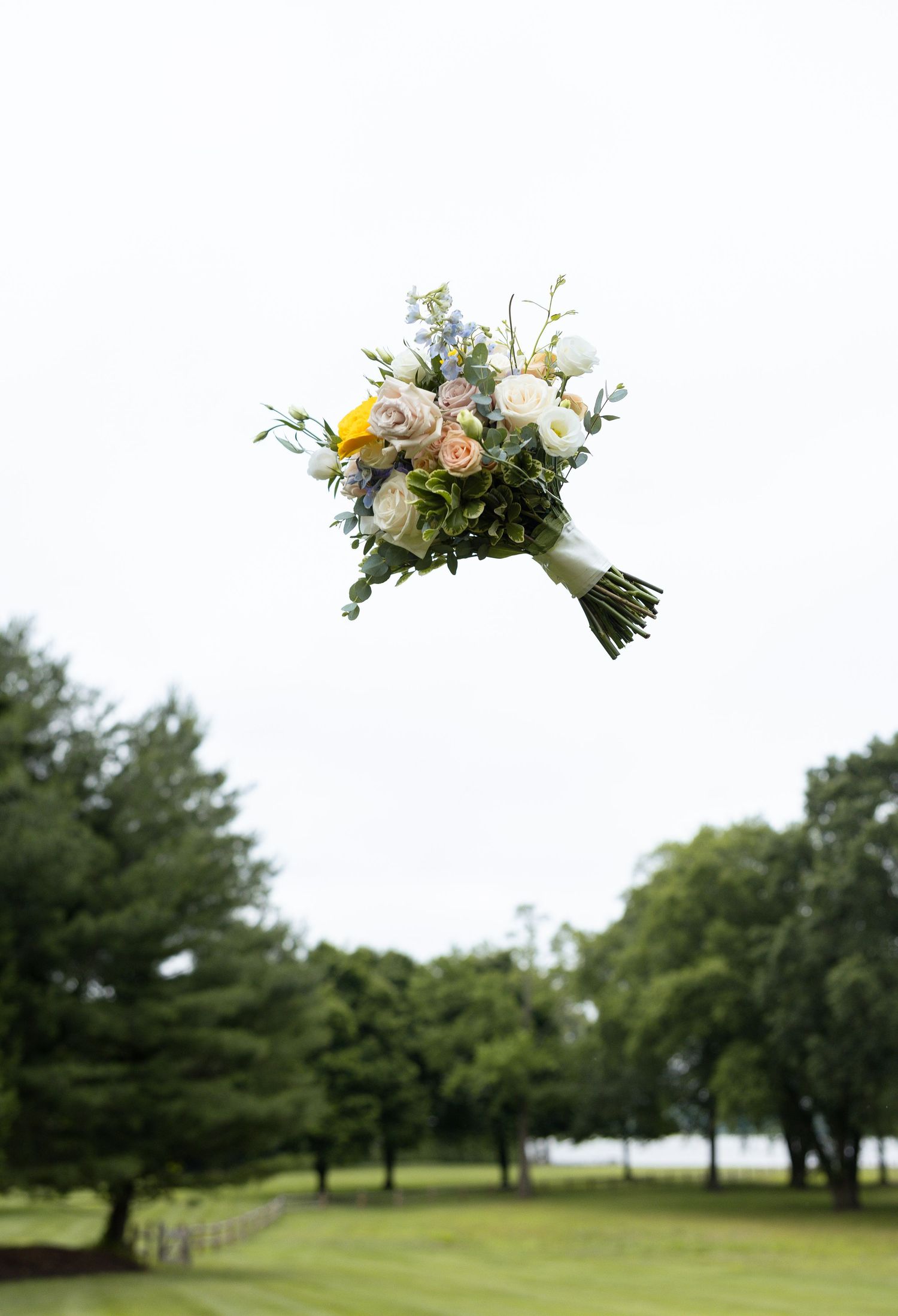A wedding bouquet with white and pink flowers against a blurred green outdoor background.