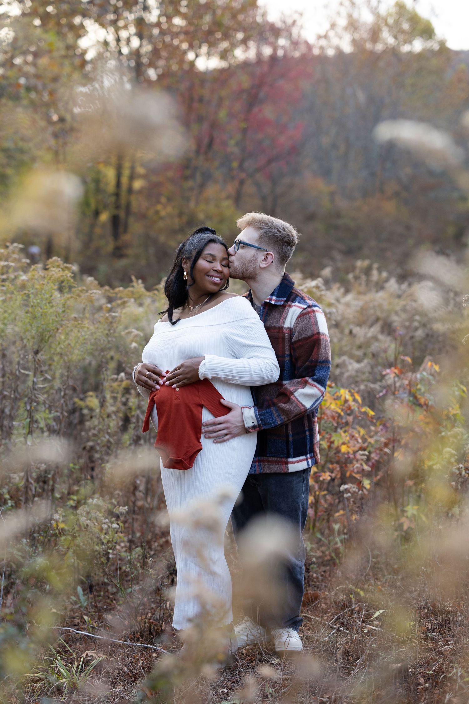 Intimate maternity portrait in fall foliage with soft bokeh effect.