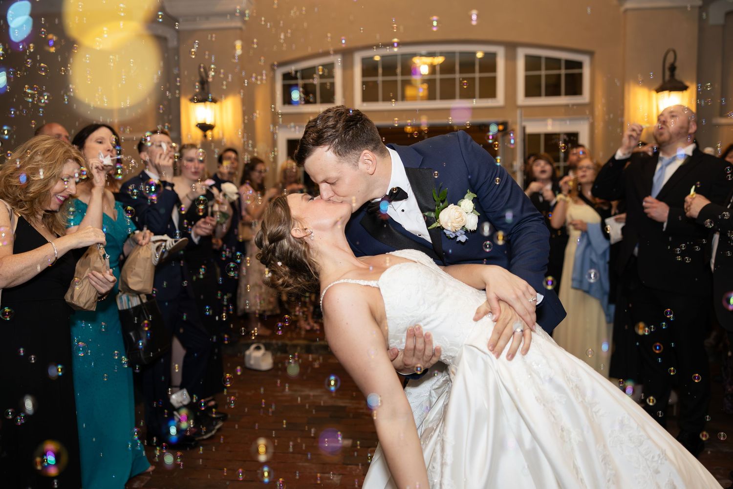 Newlyweds dancing at reception while guests blow bubbles for the grand wedding exit.