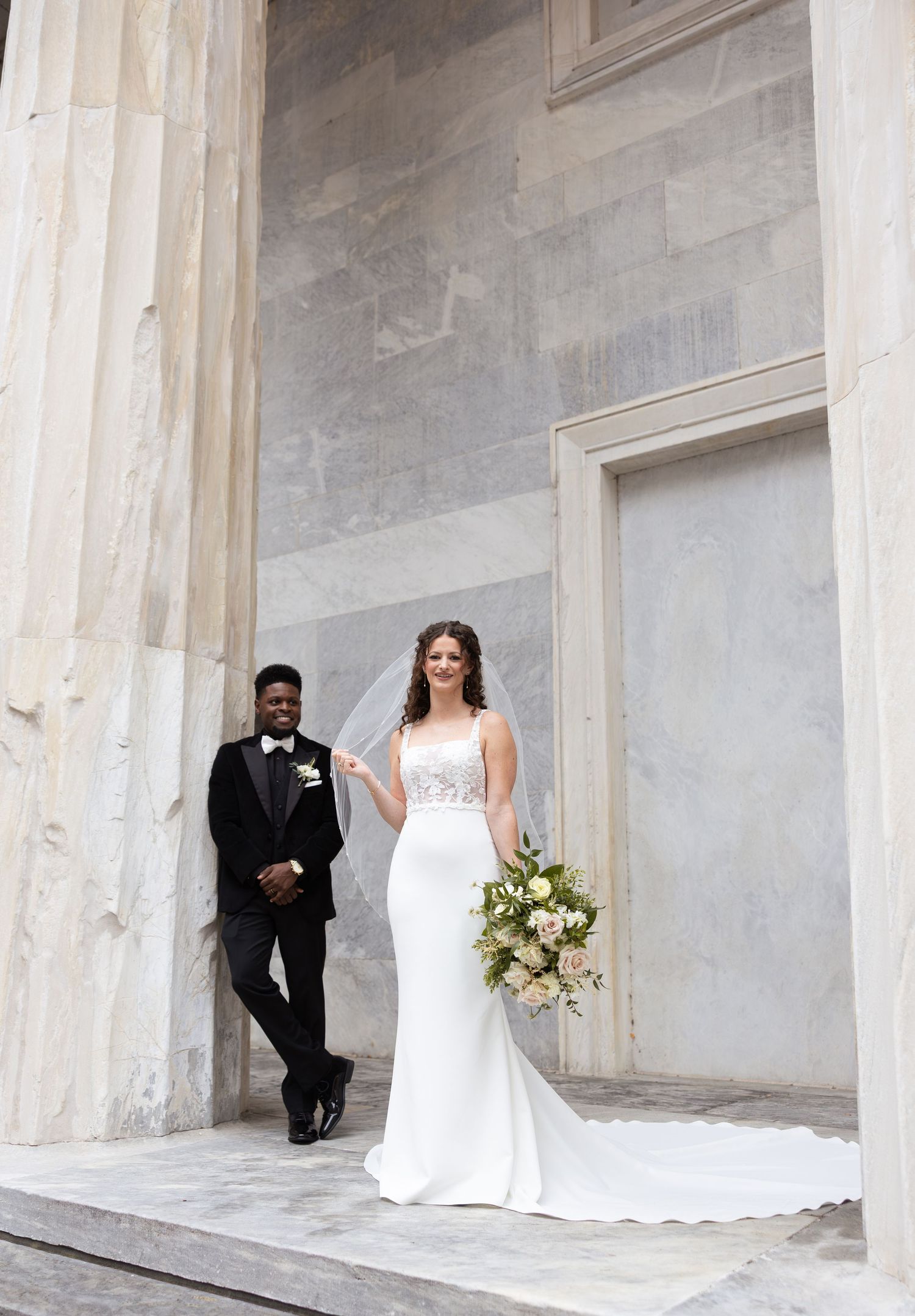 Elegant wedding photos taken between white stone columns with classical architecture.