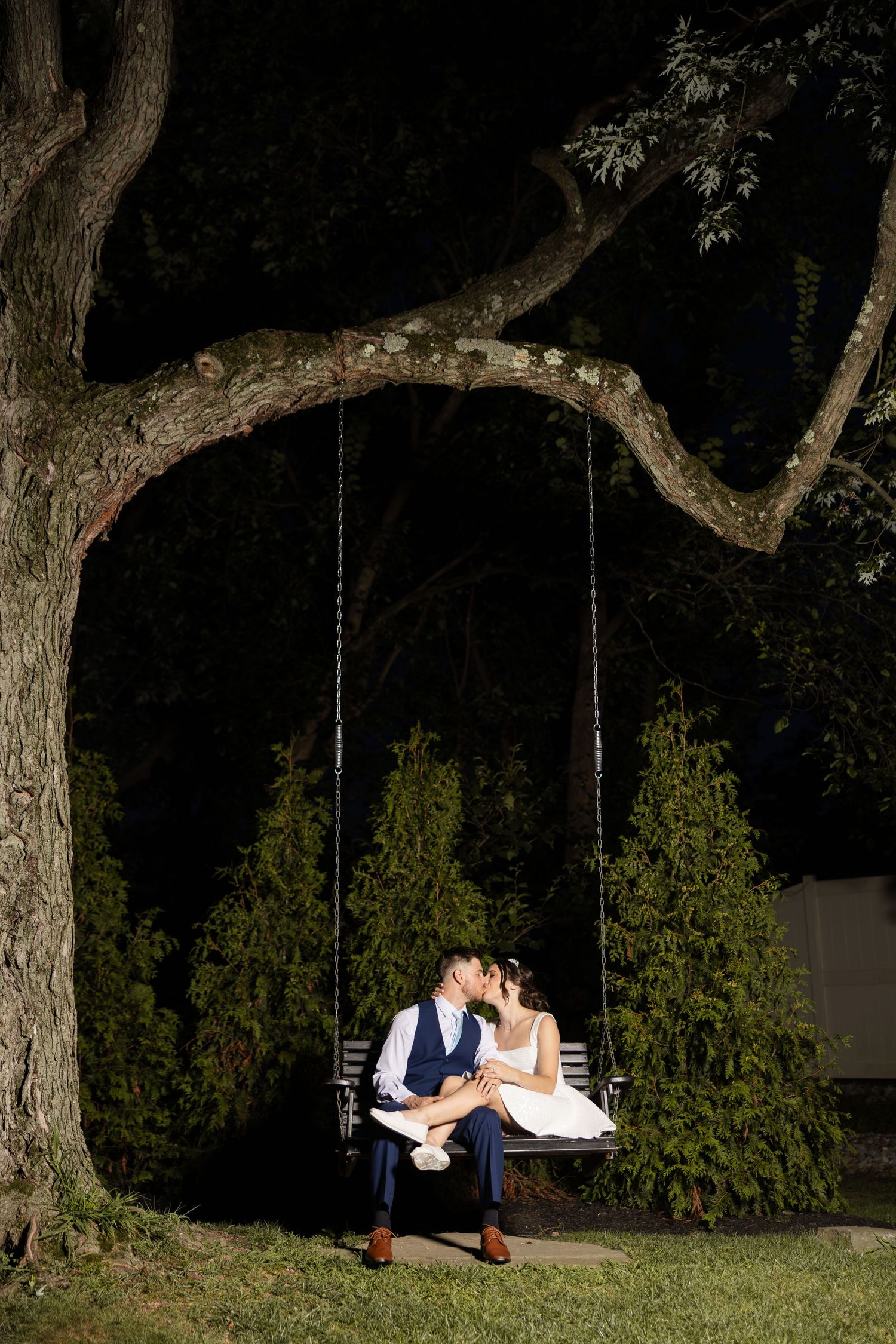 Romantic evening wedding portrait of couple sitting on a tree swing.
