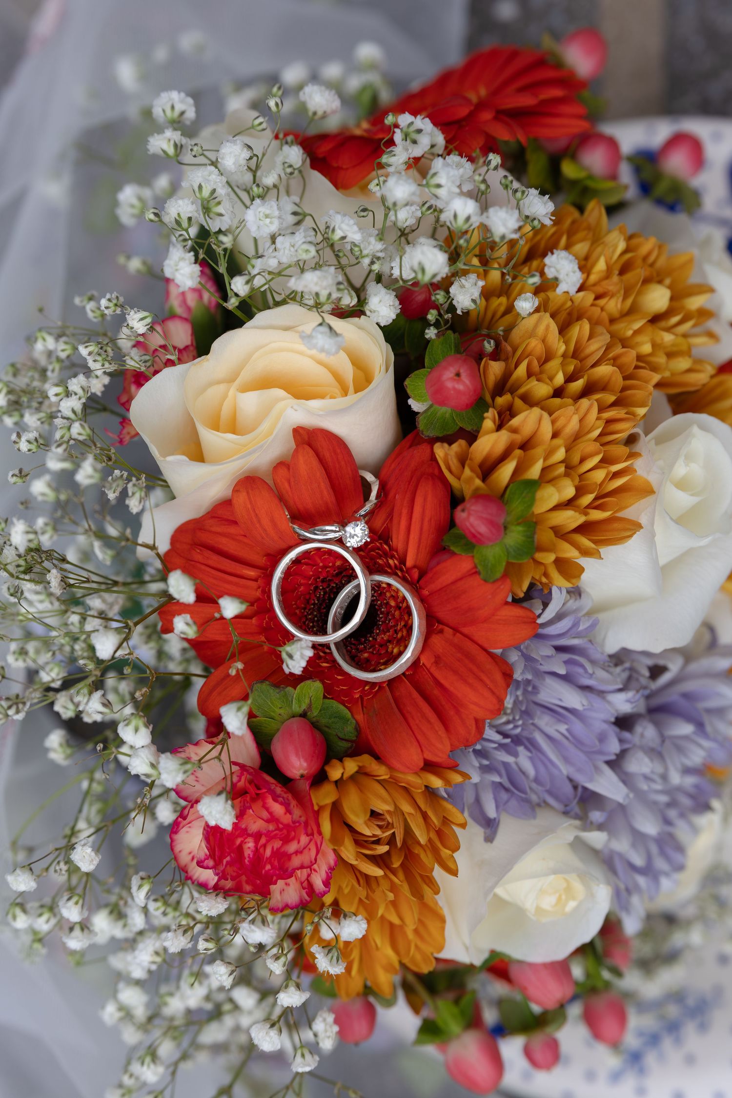 Wedding rings nestled among colorful flowers including red gerberas, orange mums and baby's breath.