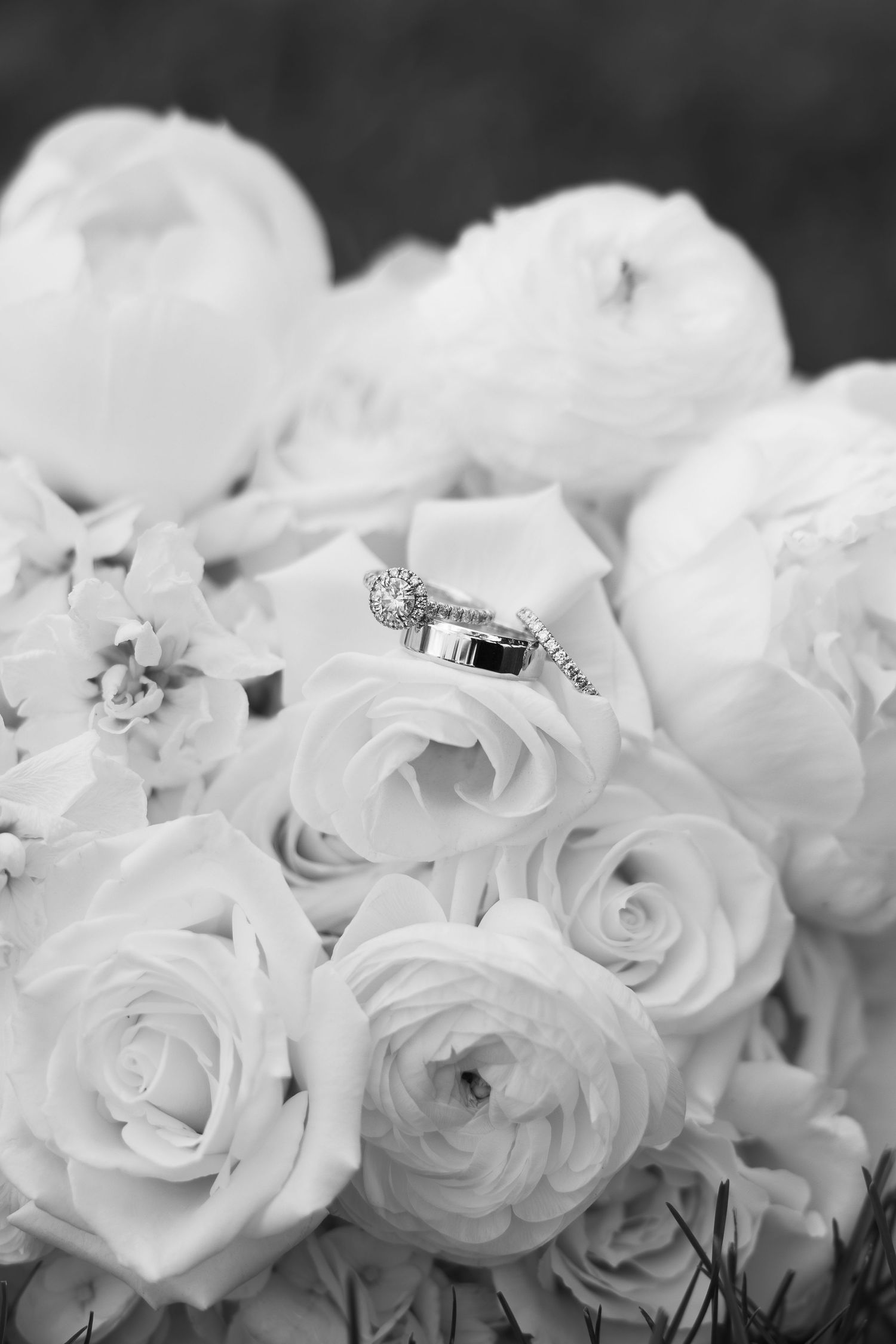 Black and white photo of wedding rings resting on a bridal bouquet of roses and peonies.