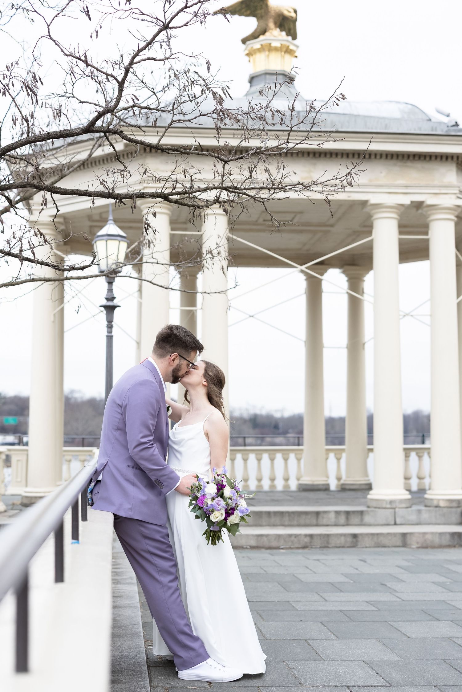 A wedding couple sharing a romantic moment by a classical white columned pavilion.