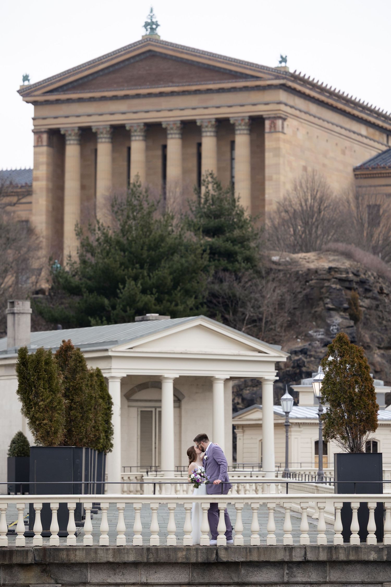 A couple sharing an intimate moment on a balcony with the Philadelphia Museum of Art in the background.