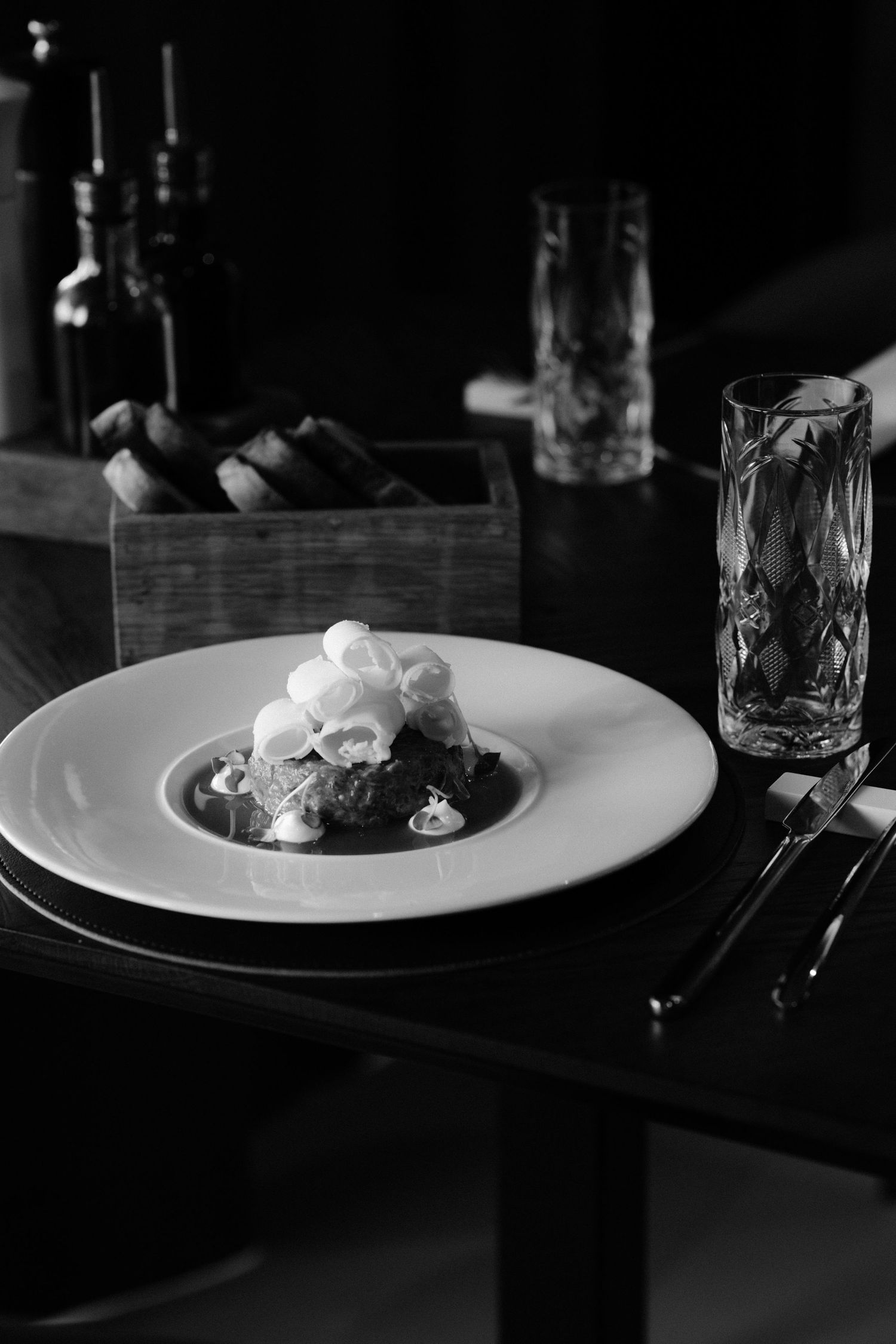 Elegant plated dishes in black and white photography on a dark wooden table.