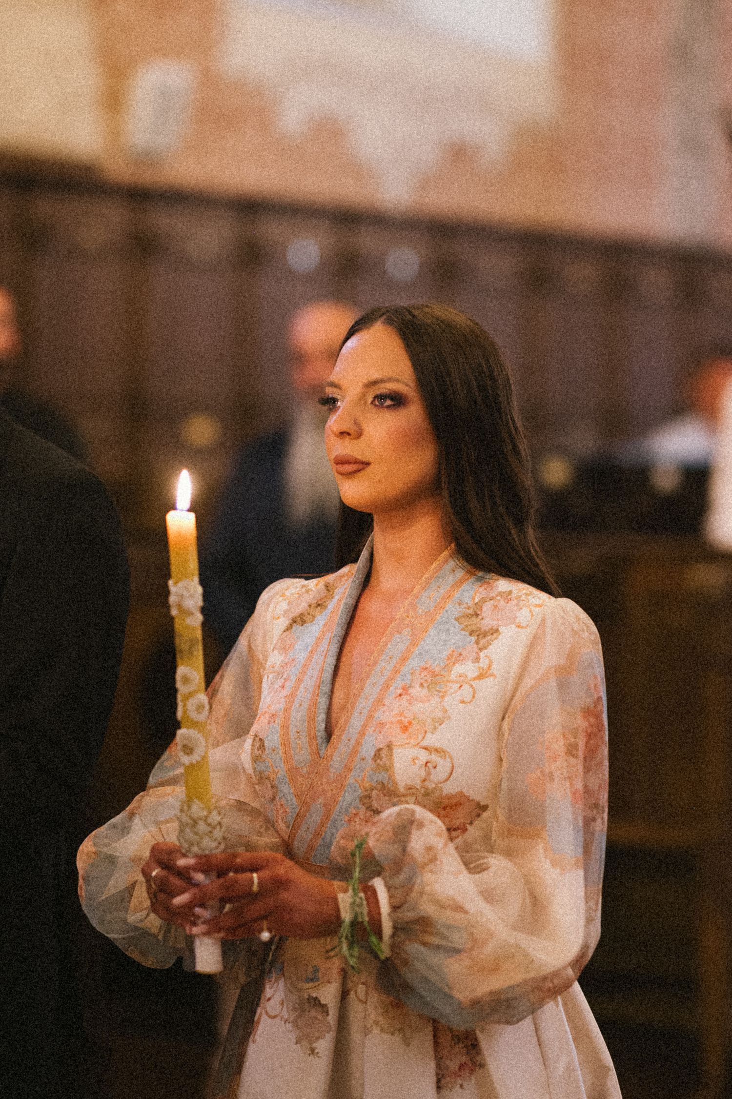 A person in a white lace dress holds a lit candle in a dimly lit church setting.