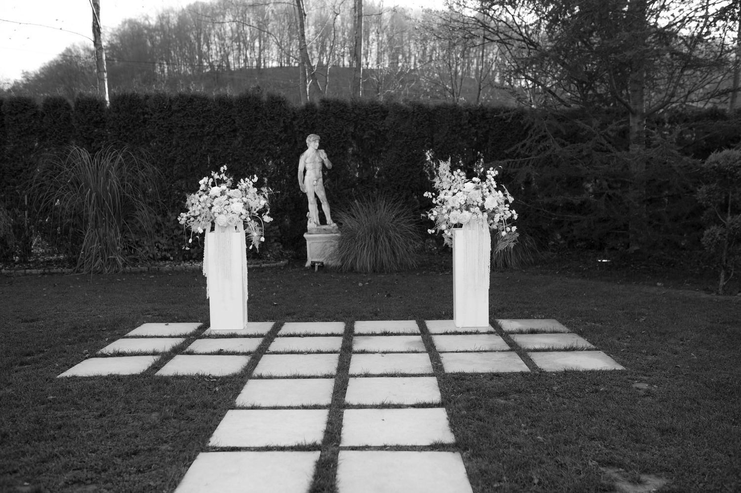 A sequence of outdoor statues and sculptures arranged in a row along a concrete pathway in a park setting.