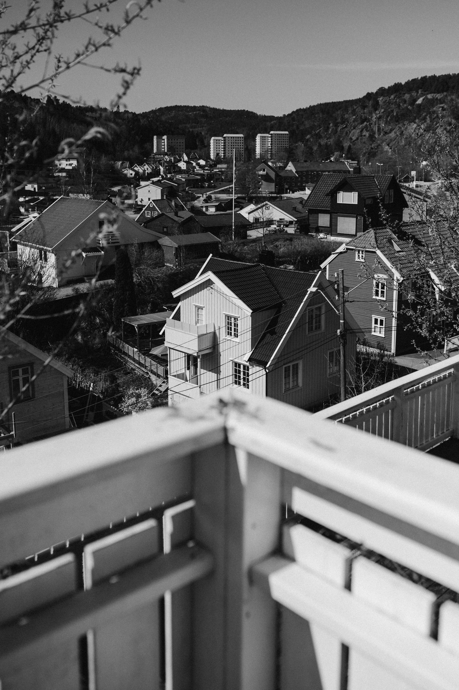 Black and white cityscape view from a balcony showing residential houses and apartment buildings nestled in hilly terrain.