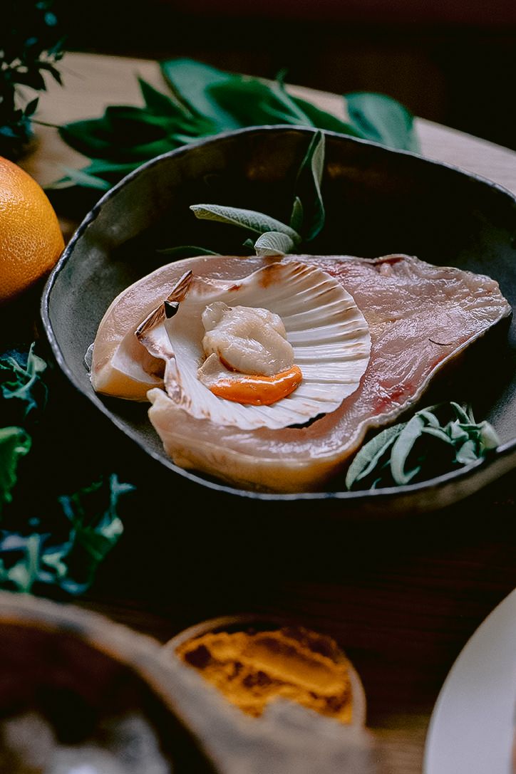Raw scallops presented on elegant dark plates with citrus accompaniments.